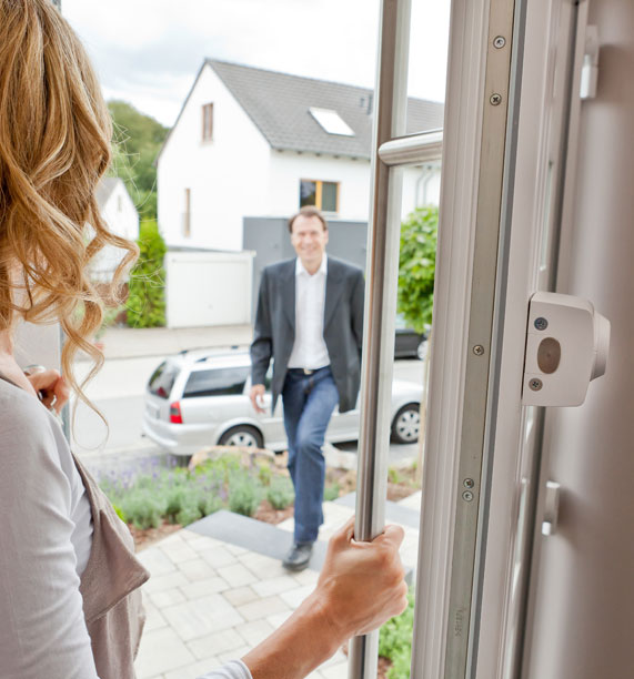 Frau öffnet Haustür mit zusätzlichem Schloss für Mann, der auf das Haus zukommt