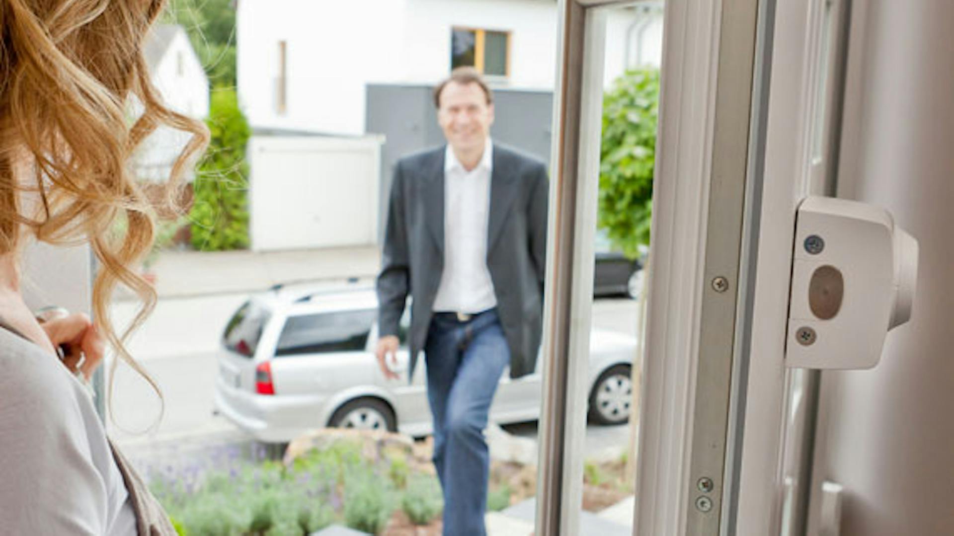 Frau öffnet Haustür mit zusätzlichem Schloss für Mann, der auf das Haus zukommt