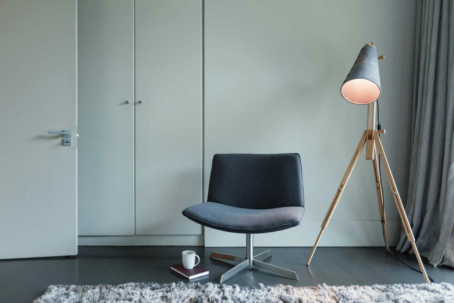 Poltrona grigia accanto ad una lampada a stelo con luce calda in una stanza con tappeto e armadio