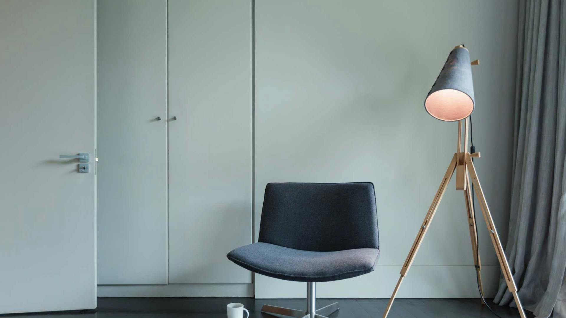 Grauer Sessel neben Stehlampe mit warmem Licht in Raum mit Teppich und Schrank