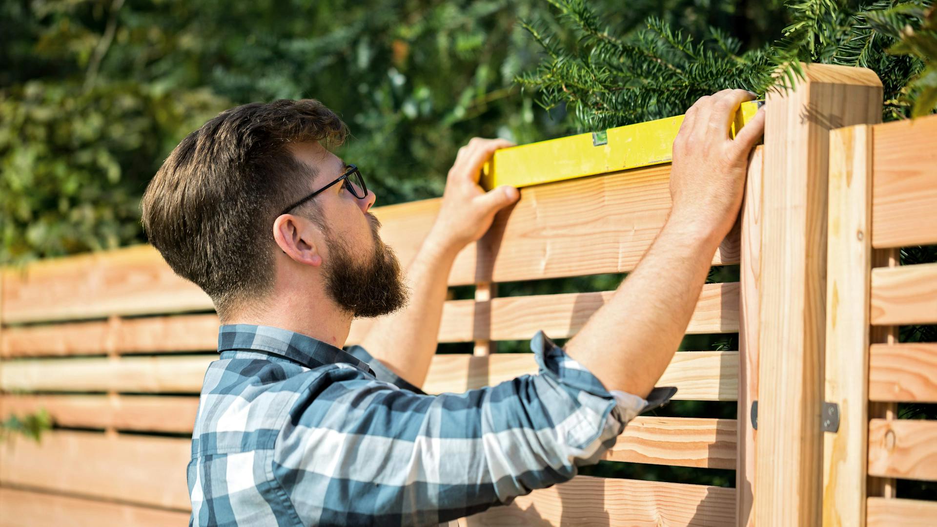 Mann baut Sichtschutz aus Holz mit Hilfe von Wasserwaage
