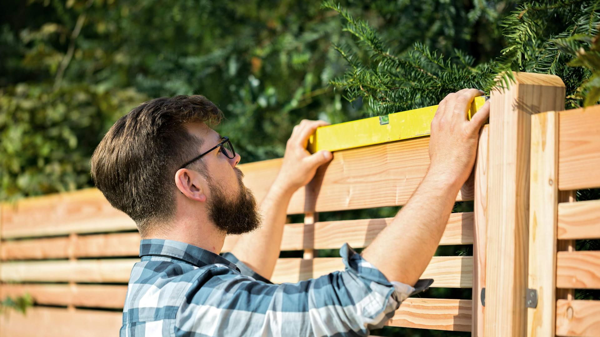 Ein Mann überprüft mit einer Wasserwaage den Sichtschutz aus Holz