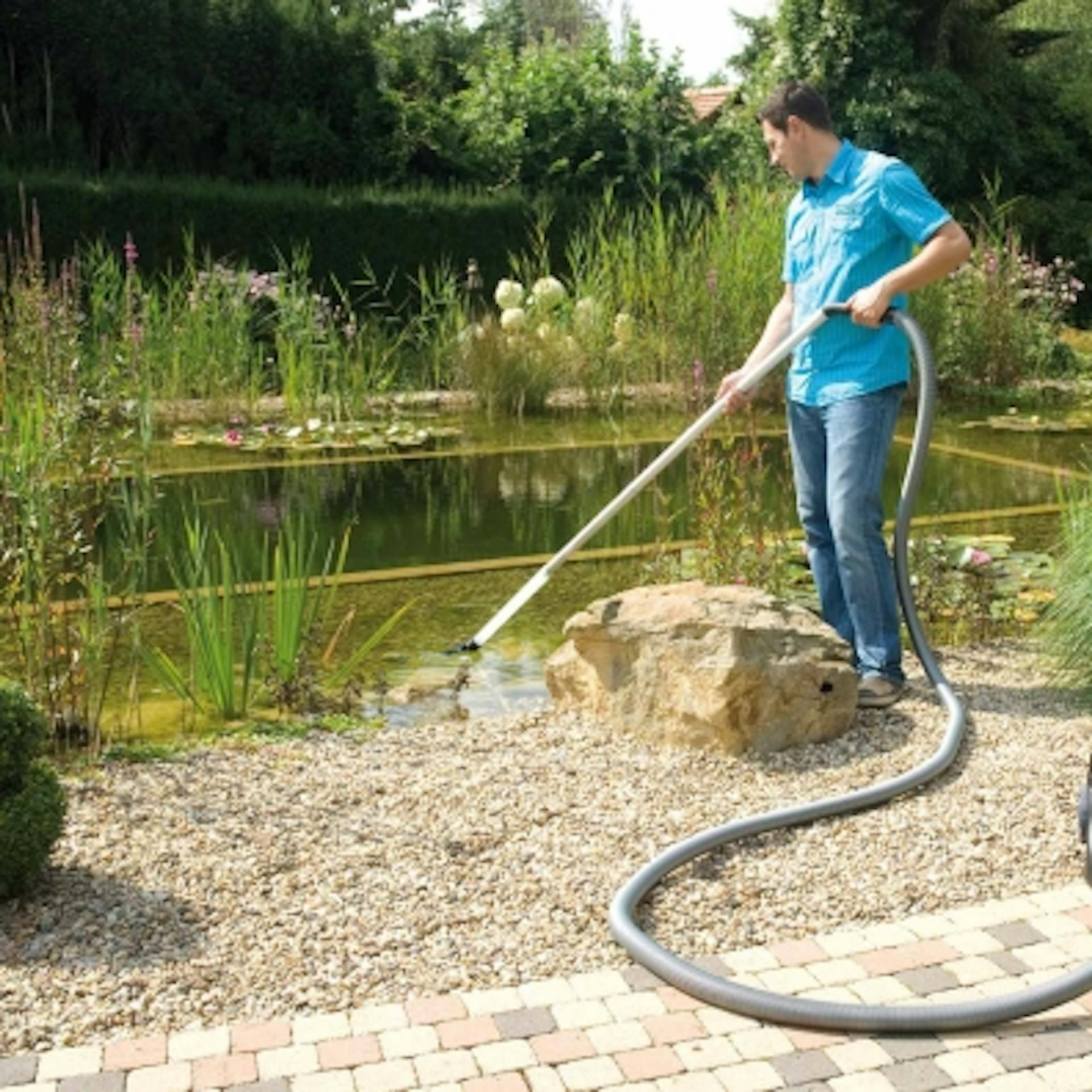 Egy kertész tóporszívóval szívja ki az algákat a kerti tóból.