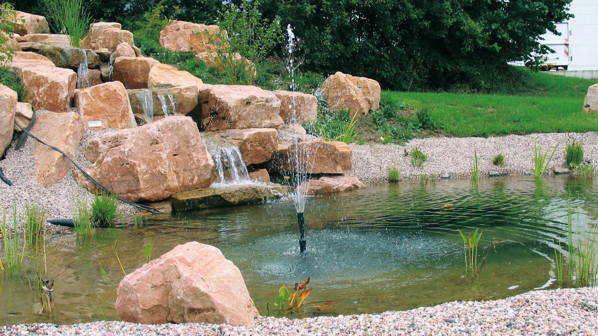 Wasserfall fließt über Stufen in Teich mit Springbrunnen.