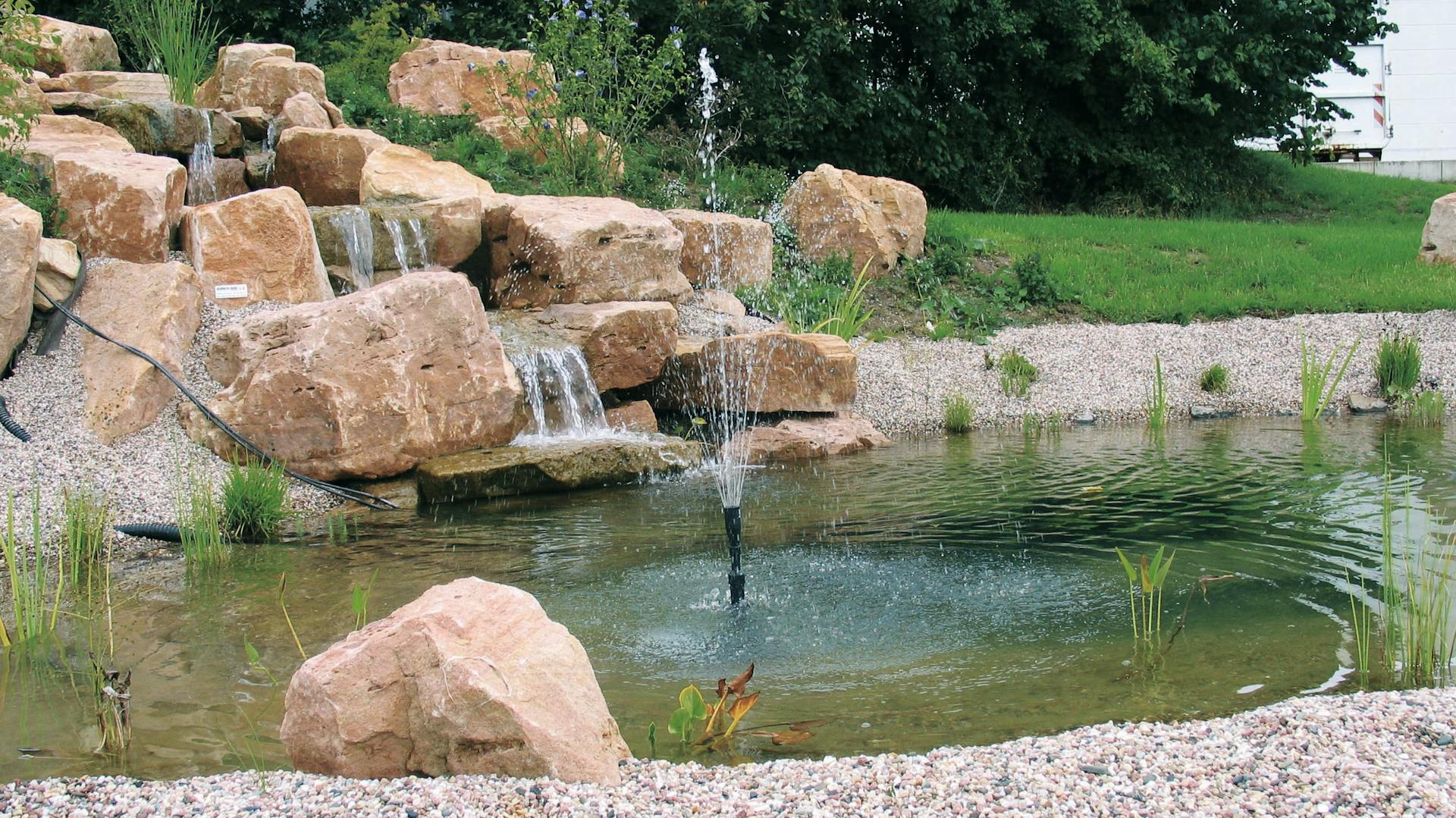Wasserfall fließt über Stufen in Teich mit Springbrunnen.