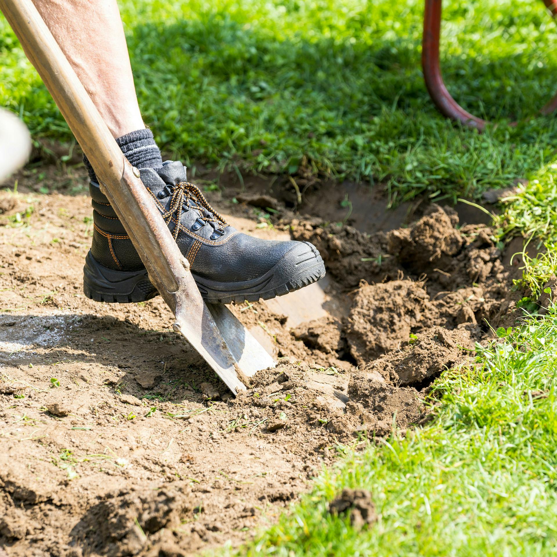 Person hebt Boden in Garten mit Spaten aus.