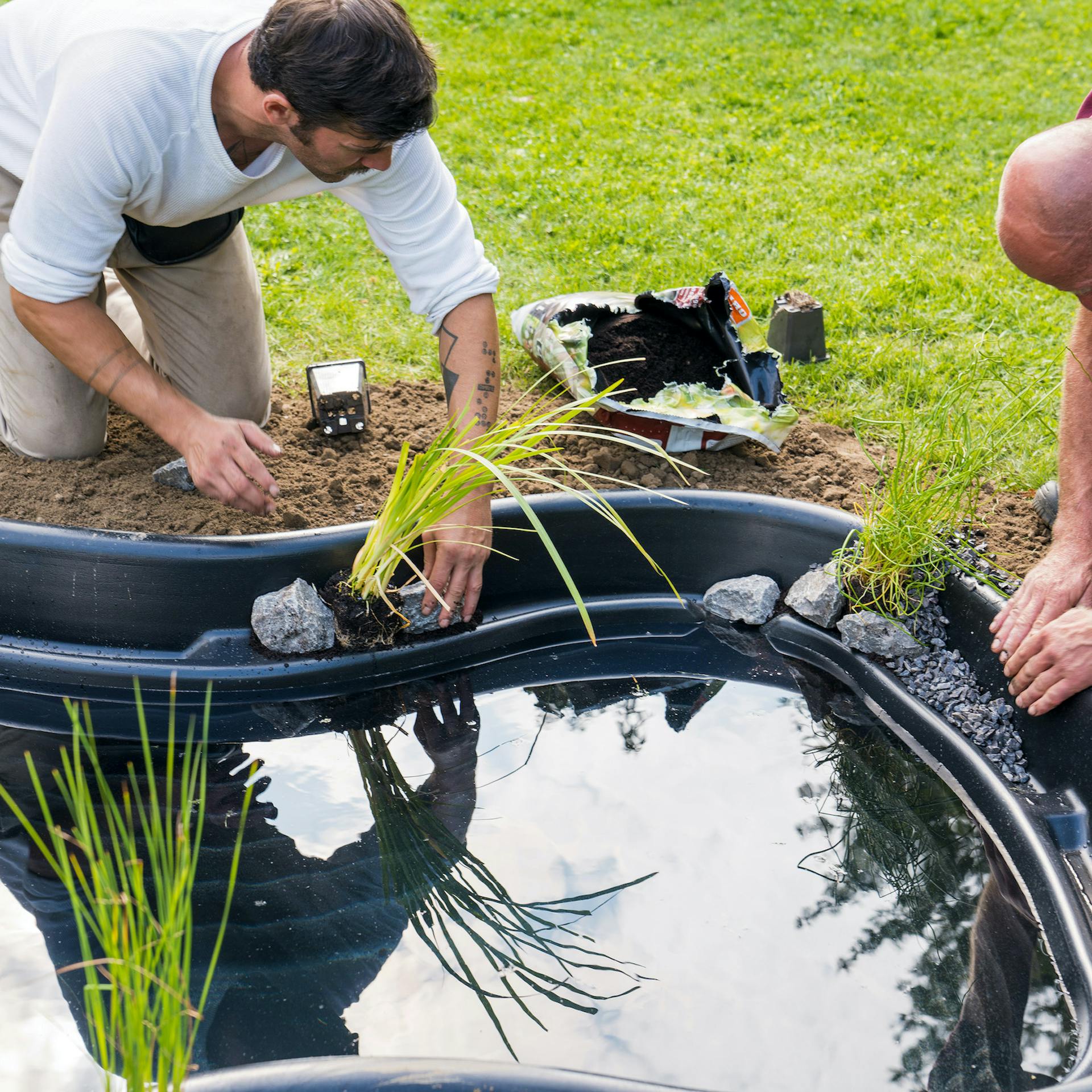 Heimwerker setzen Teichpflanzen in Fertigteich ein.
