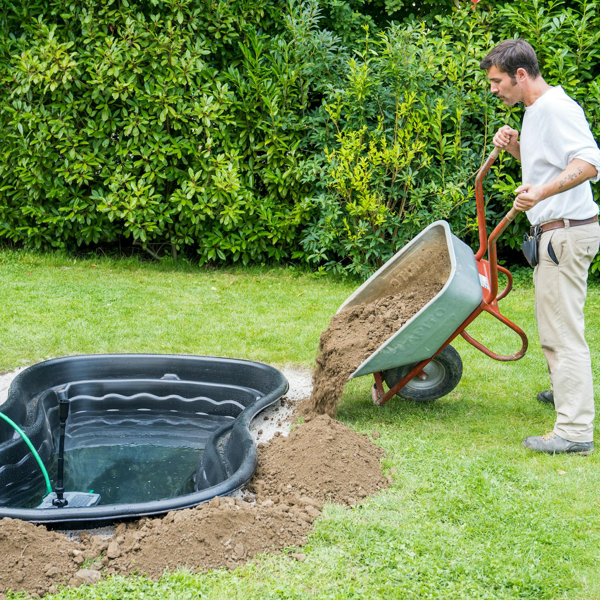Mann füllt Teichrand mit Erde auf