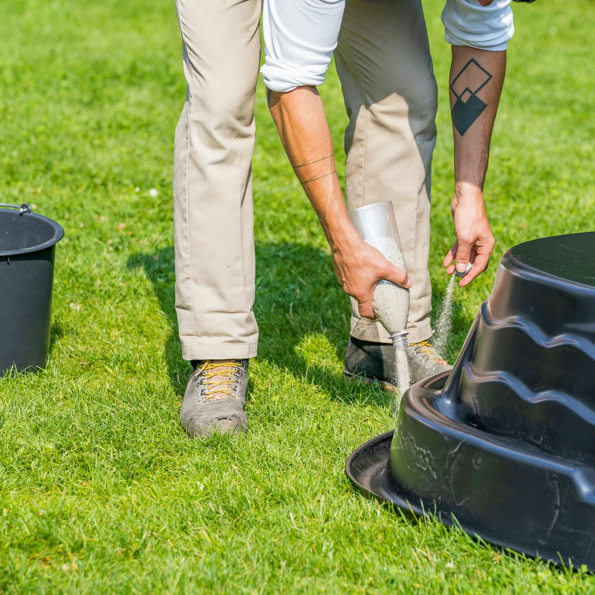 Person markiert Umrisse von umgedrehten Teichbecken auf Rasen mit Sand.
