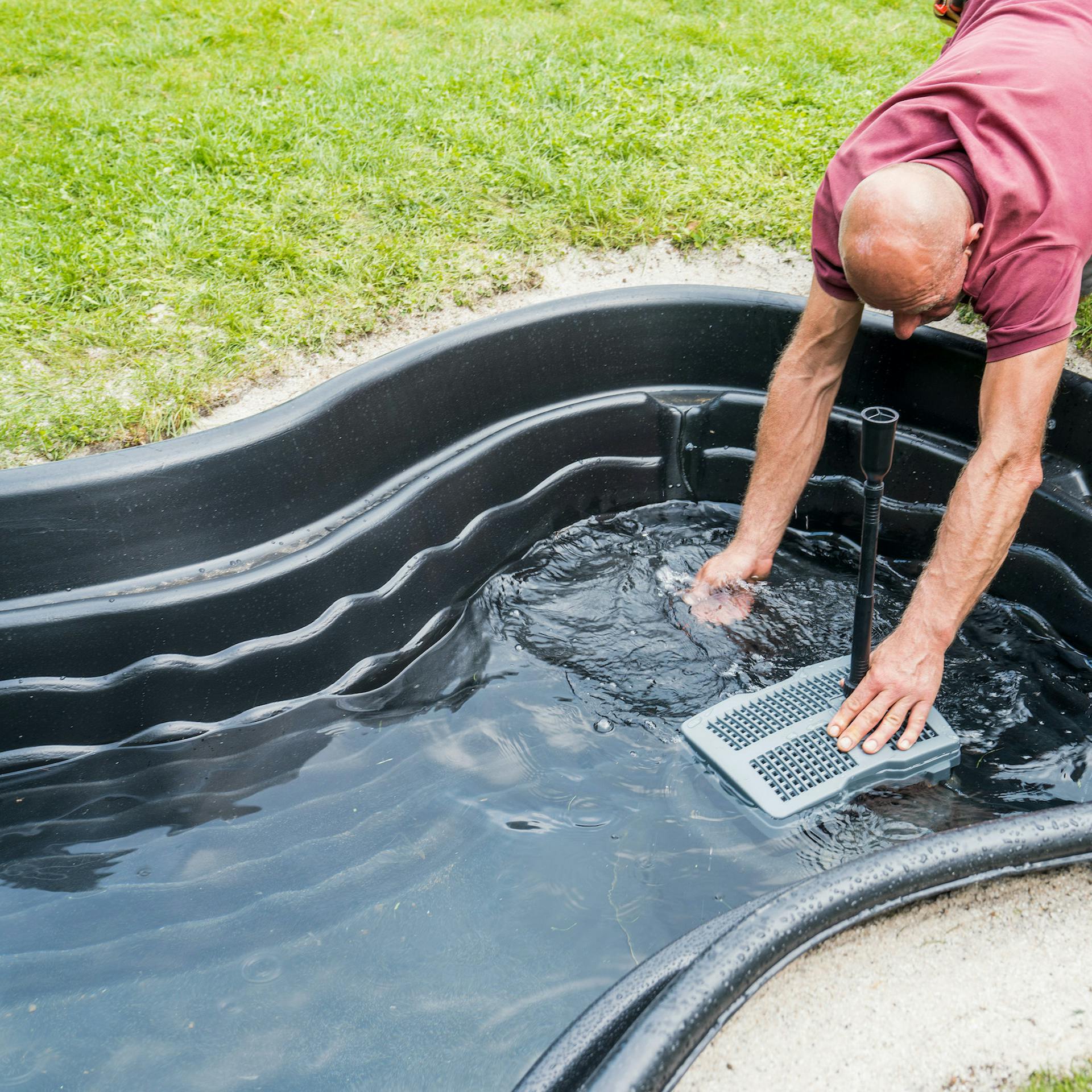 Heimwerker setzen Teichpumpe in mit Wasser befüllten Fertigteich ein.