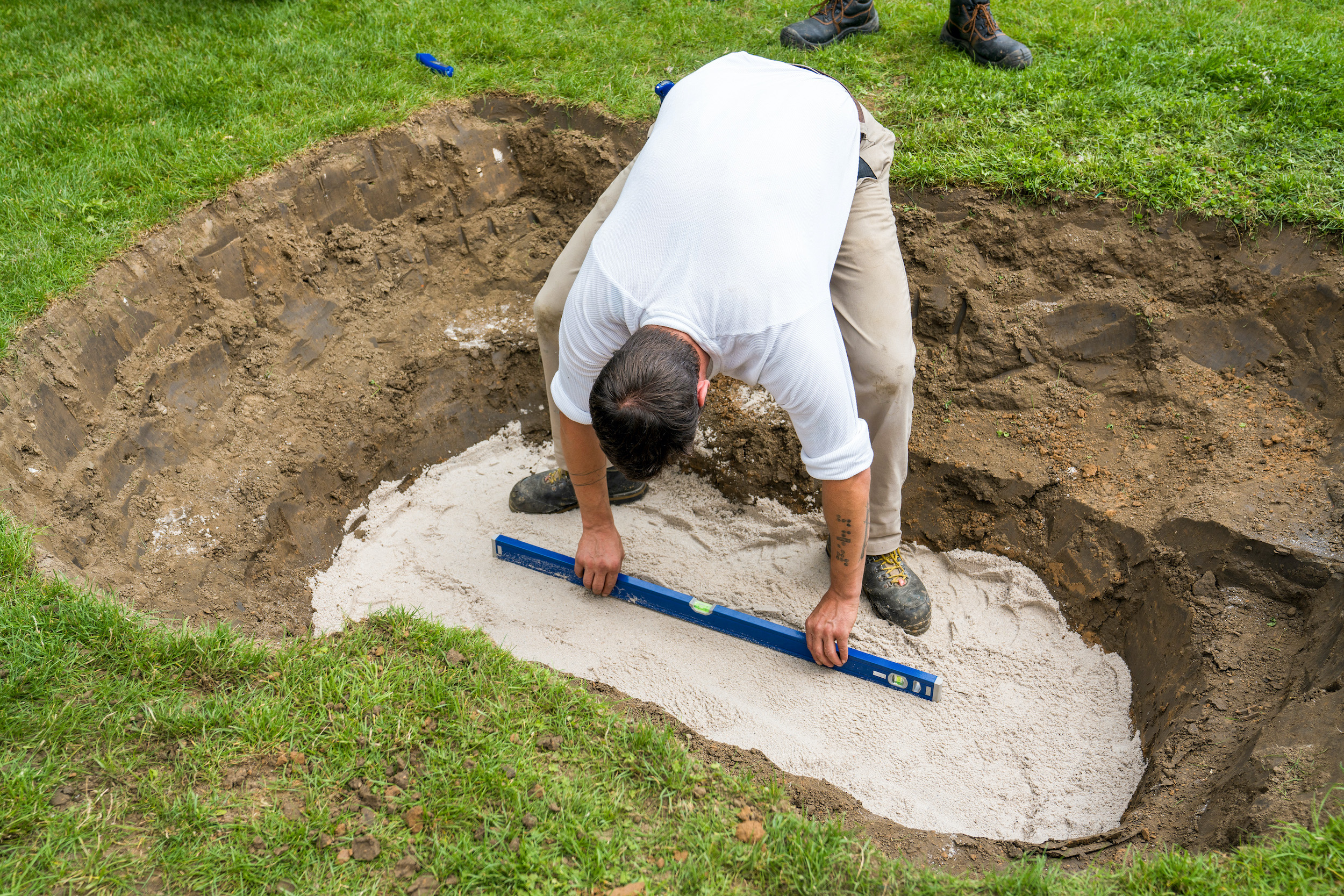 Domácí kutil kontroluje vodorovné vyrovnání vrstvy písku pomocí vodováhy