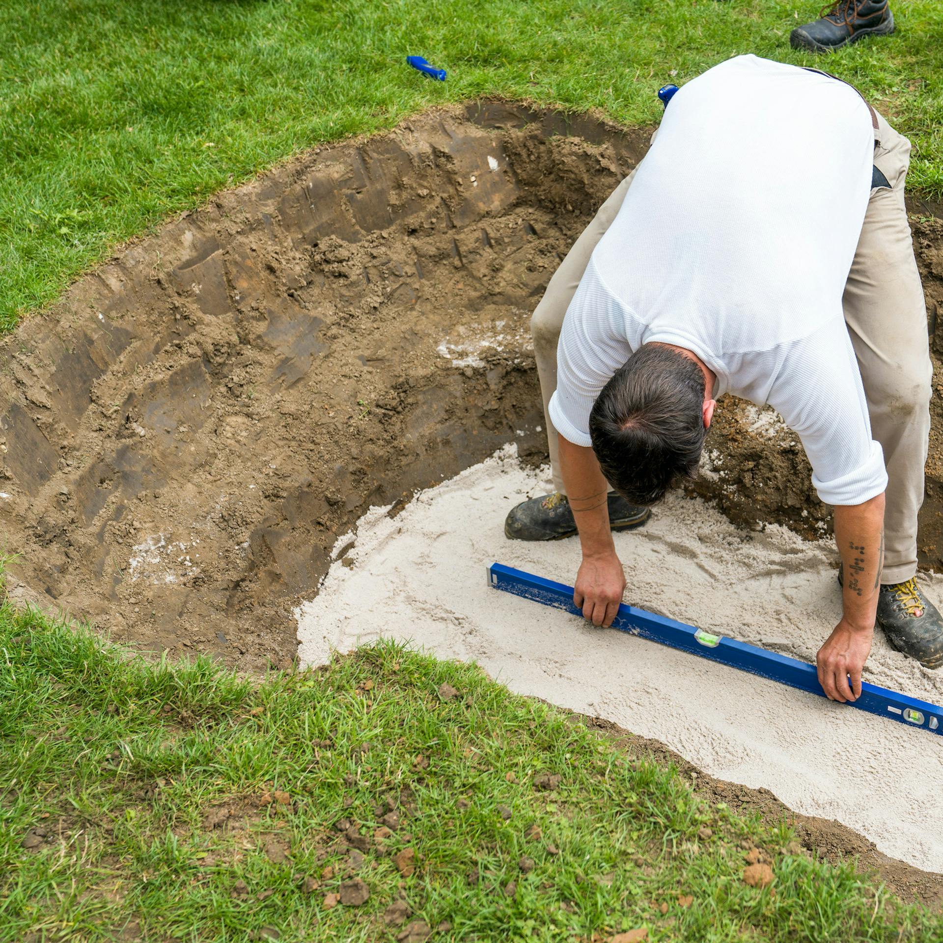 Heimwerker prüft waagerechte Ausrichtung der Sandschicht mit Wasserwaage.
