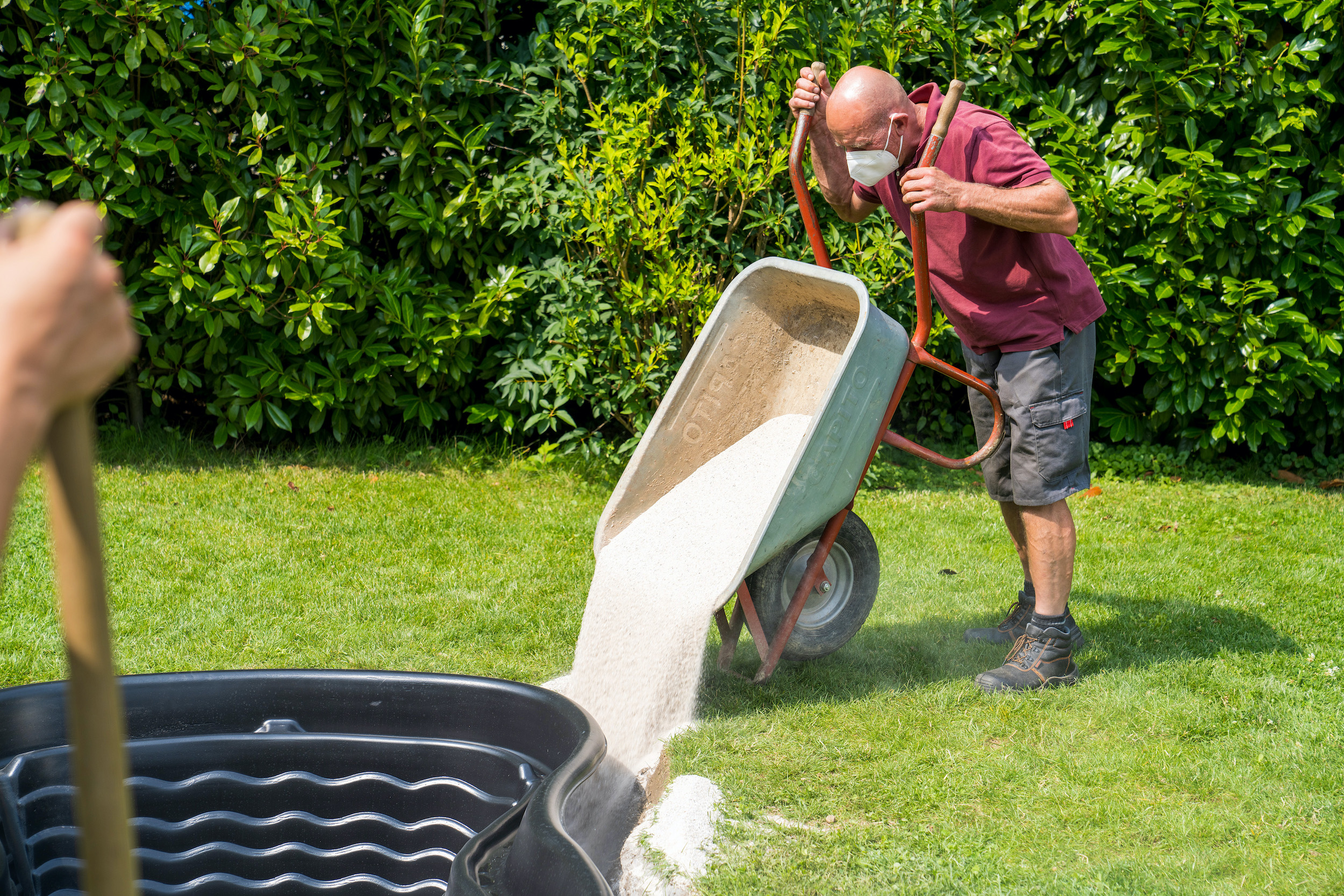 Muž vyklápí písek mezi jezírkovou skořepinu a jámu