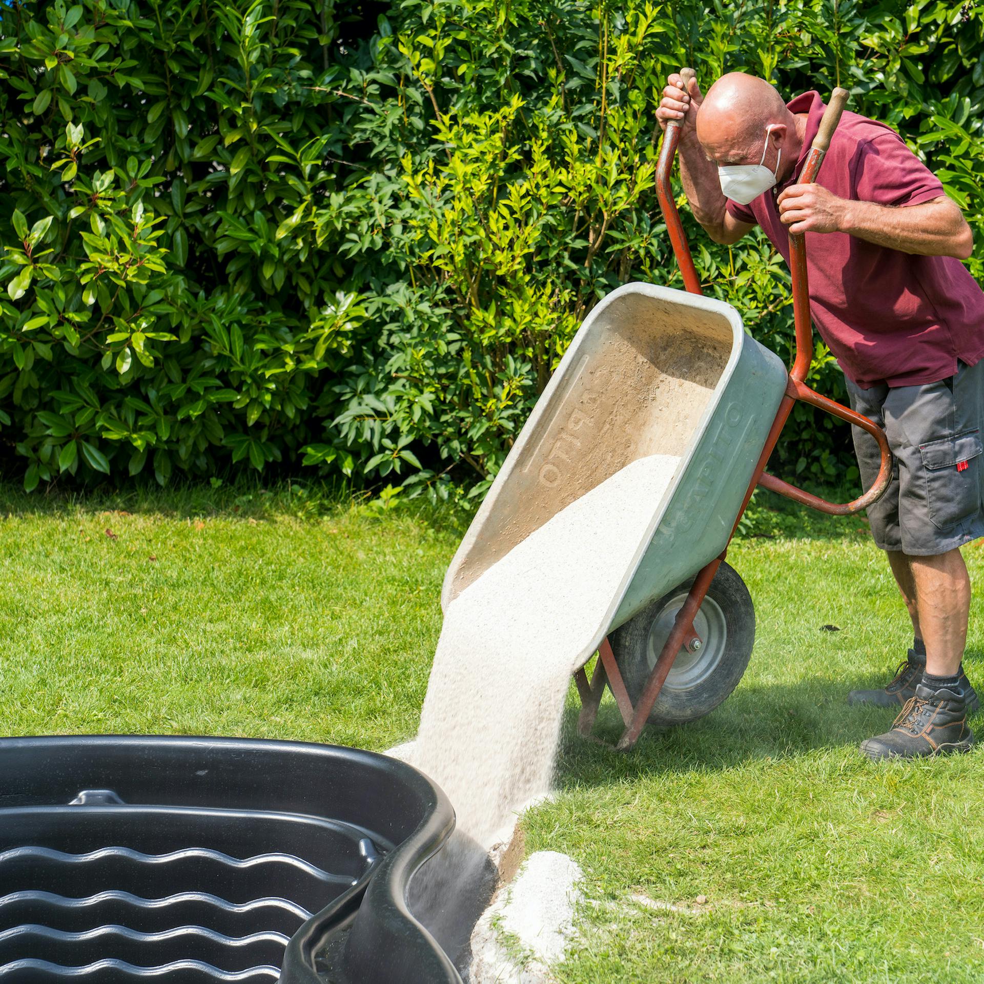 Mann kippt Sand zwischen Teichbecken und Grube.
