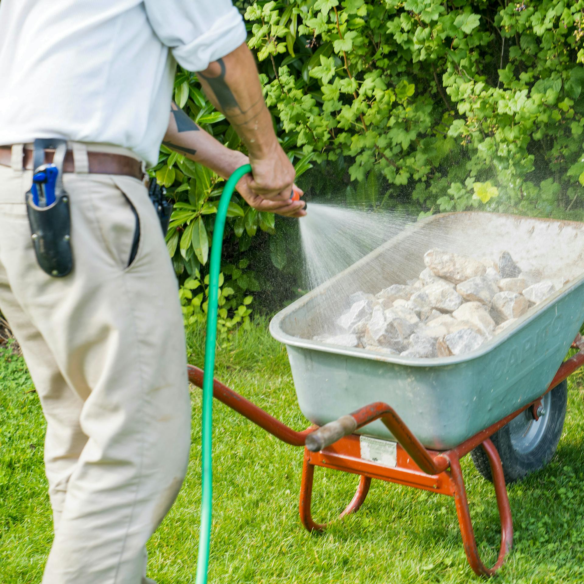 Mann reinigt Steine mit Gartenschlauch in der Schubkarre