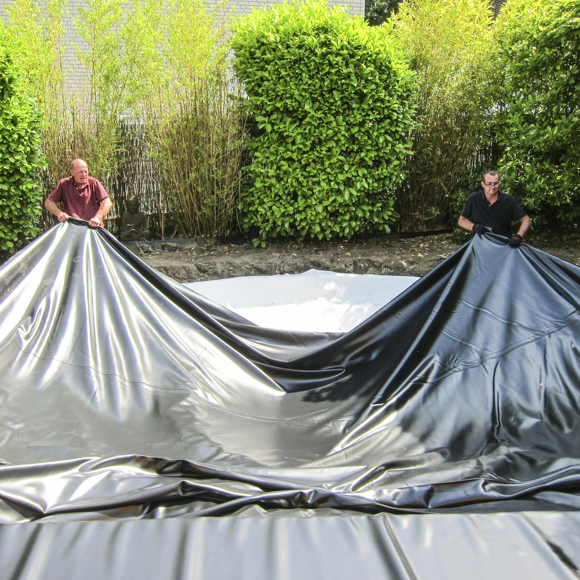 Zwei Personen breiten eine Teichfolie über einem Teichaushub aus