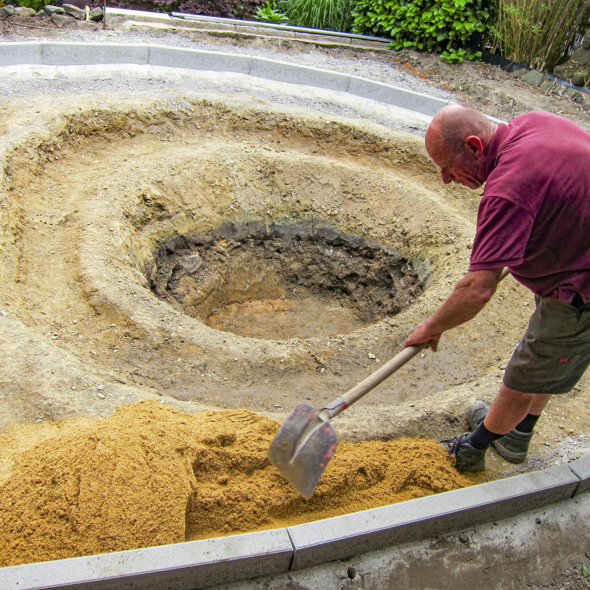 Handwerker bedeckt die äußere Teichzone mit Sand.