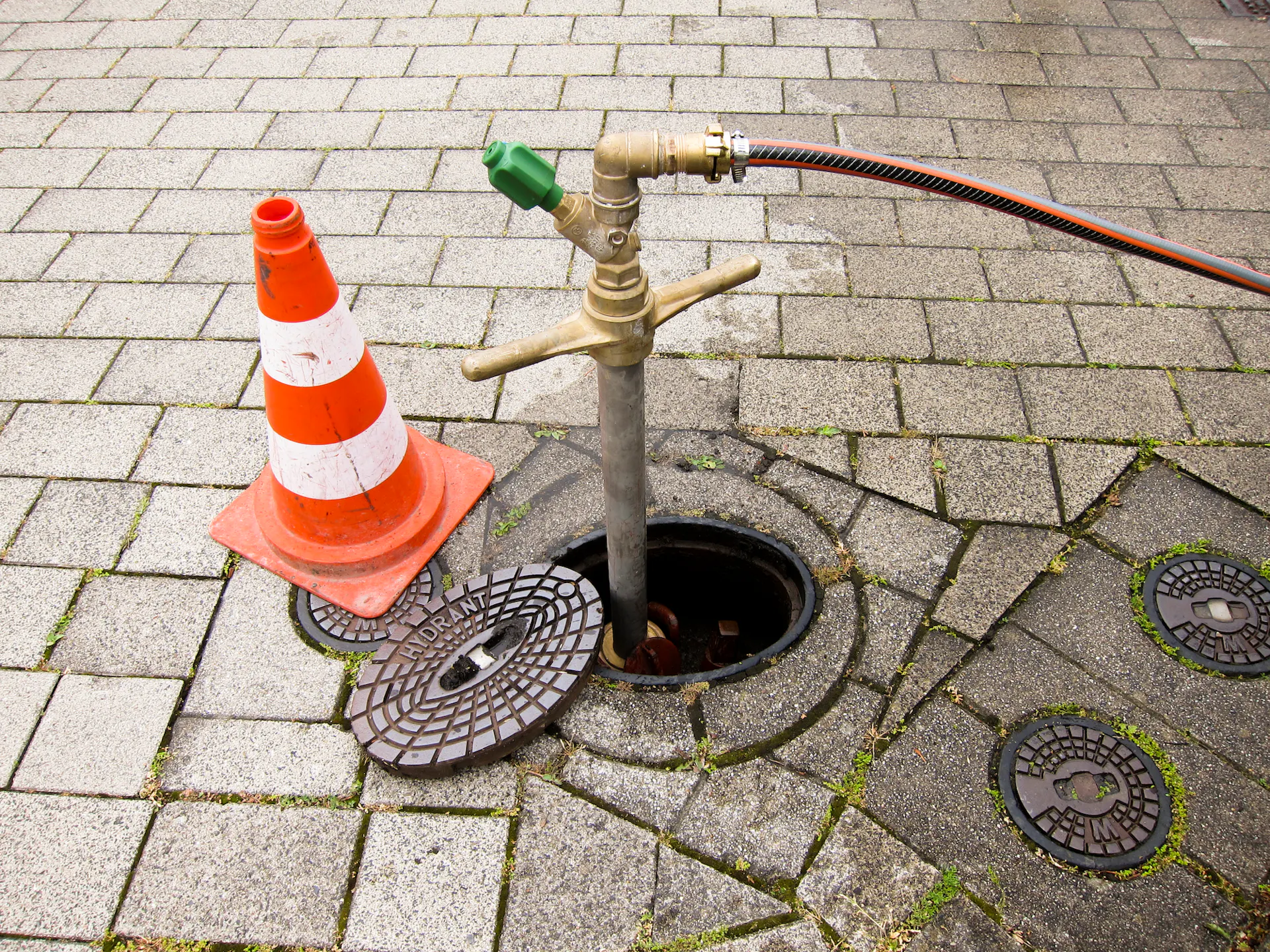 K hydrantu je pripojená záhradná hadica a vľavo je vodiaci kužeľ.