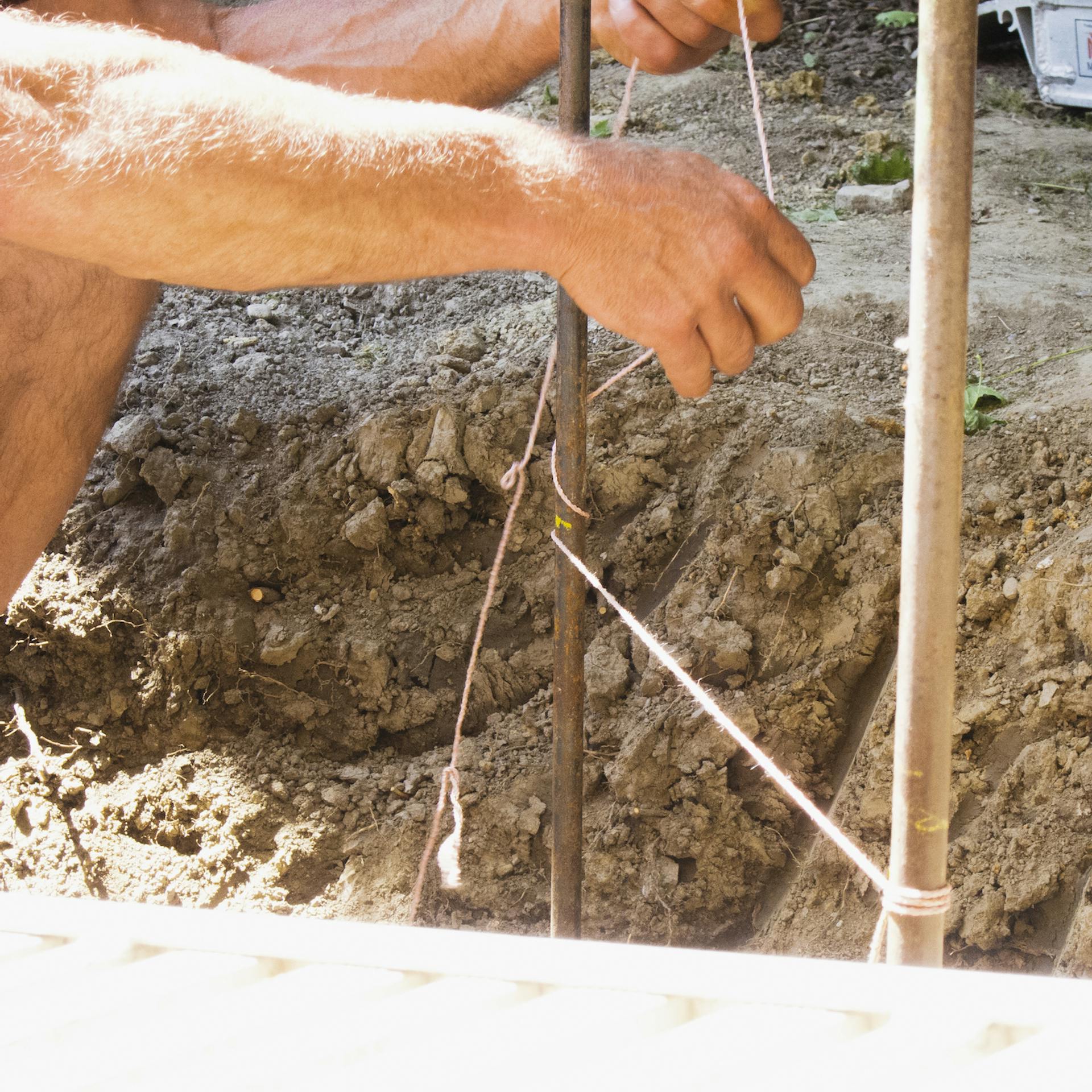 Heimwerker fädelt die Maurerschnur um die Eisenpinne herum.