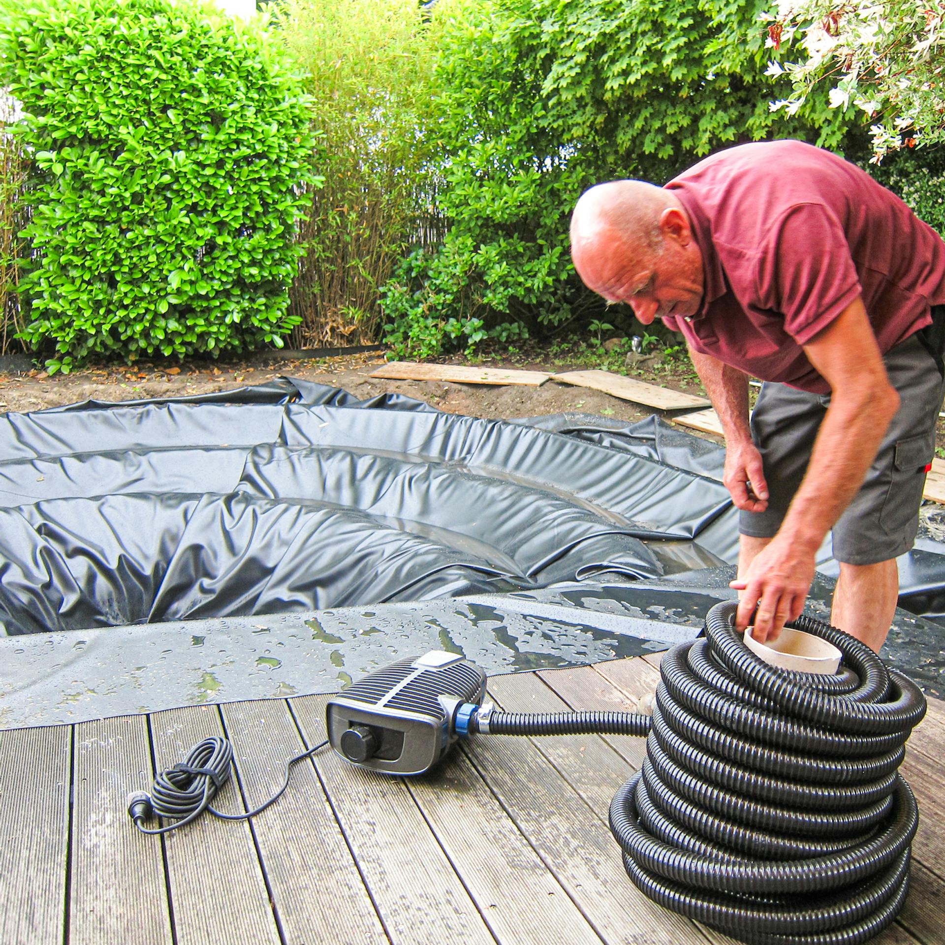 Dolgozó ember feltekeri a tószivattyú tömlőjét.