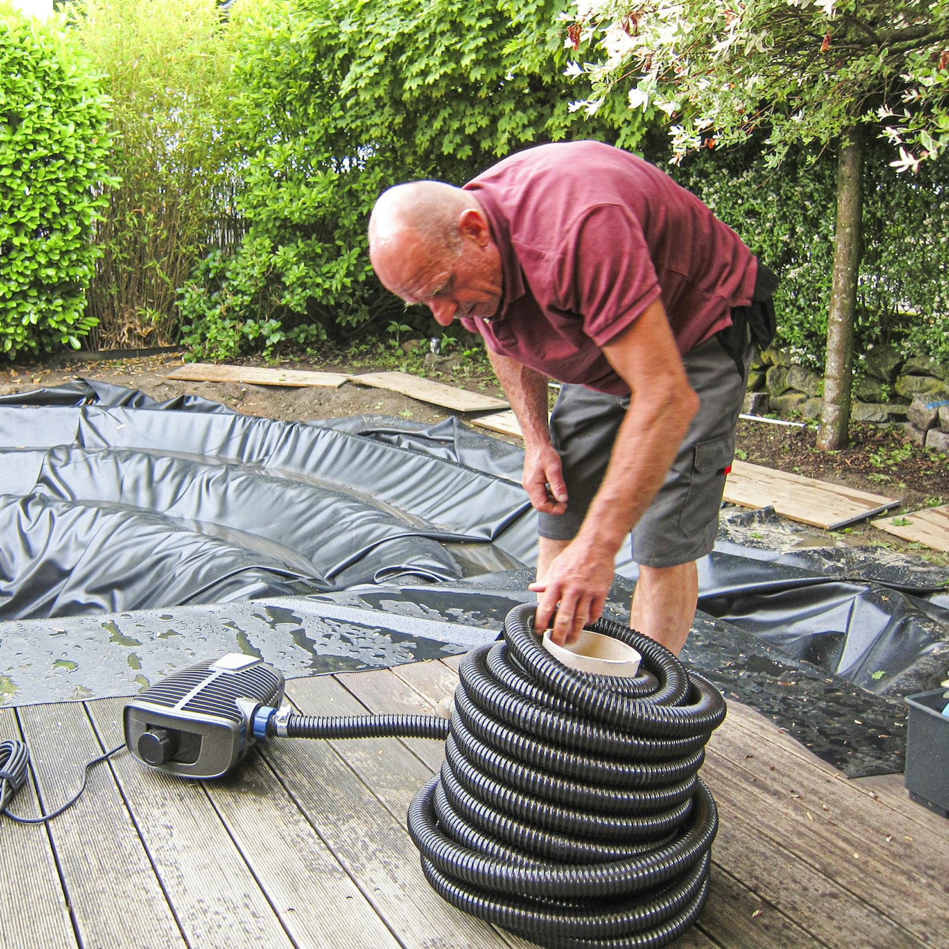 Handwerker rollt den Schlauch der Teichpumpe auf.