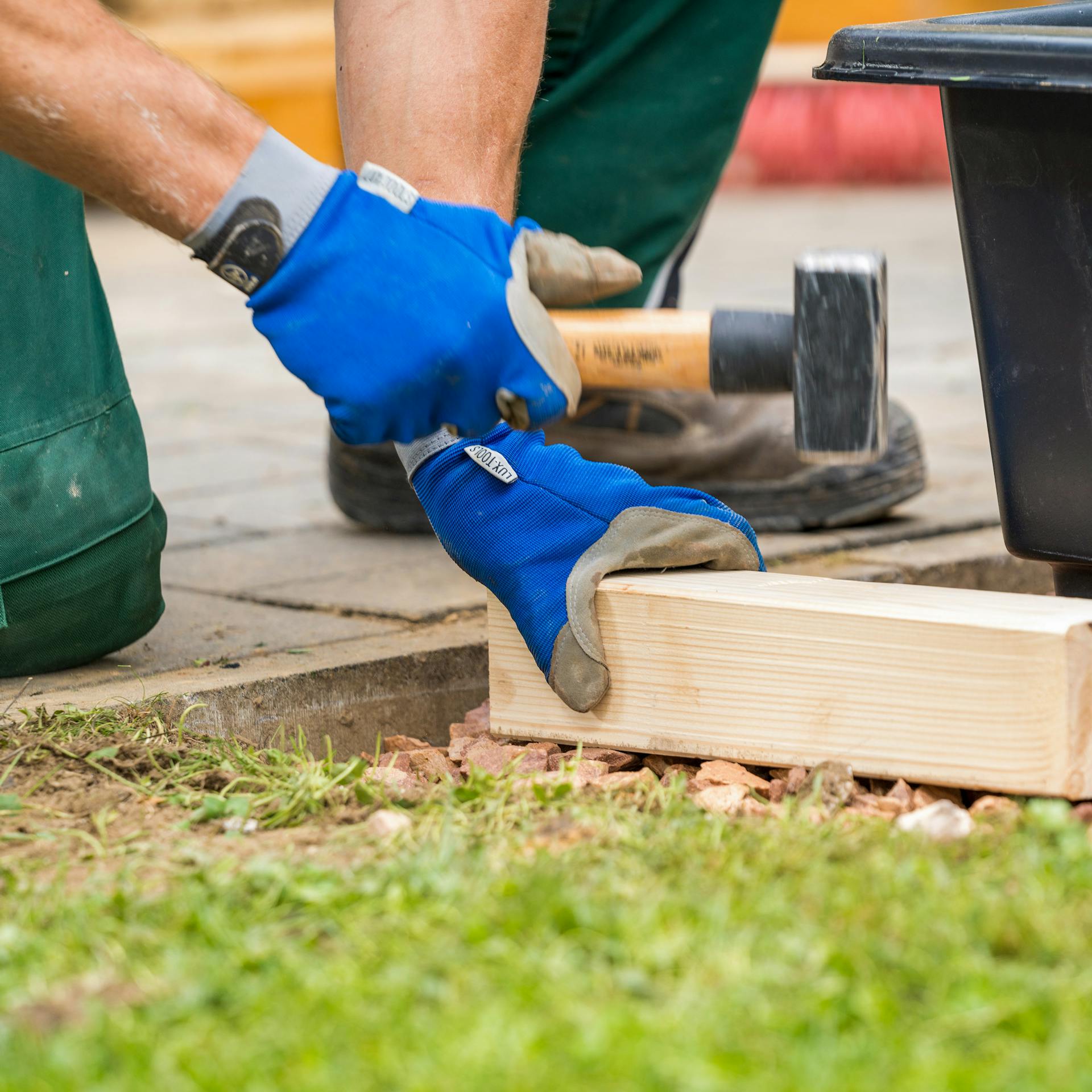 Heimwerker verdichtet Splitt mithilfe von Hammer und Holzscheit.