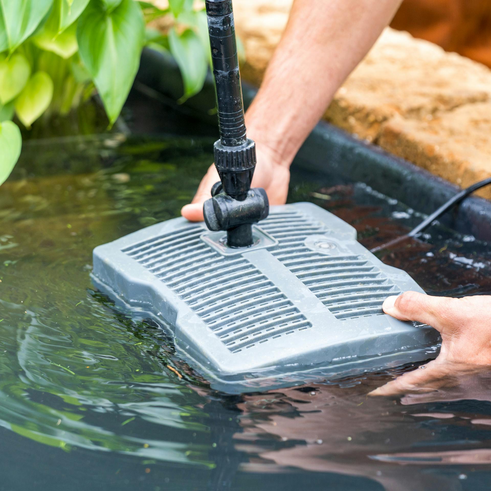 Heimwerker setzt Tauchpumpe in fertig gestellten Teich.