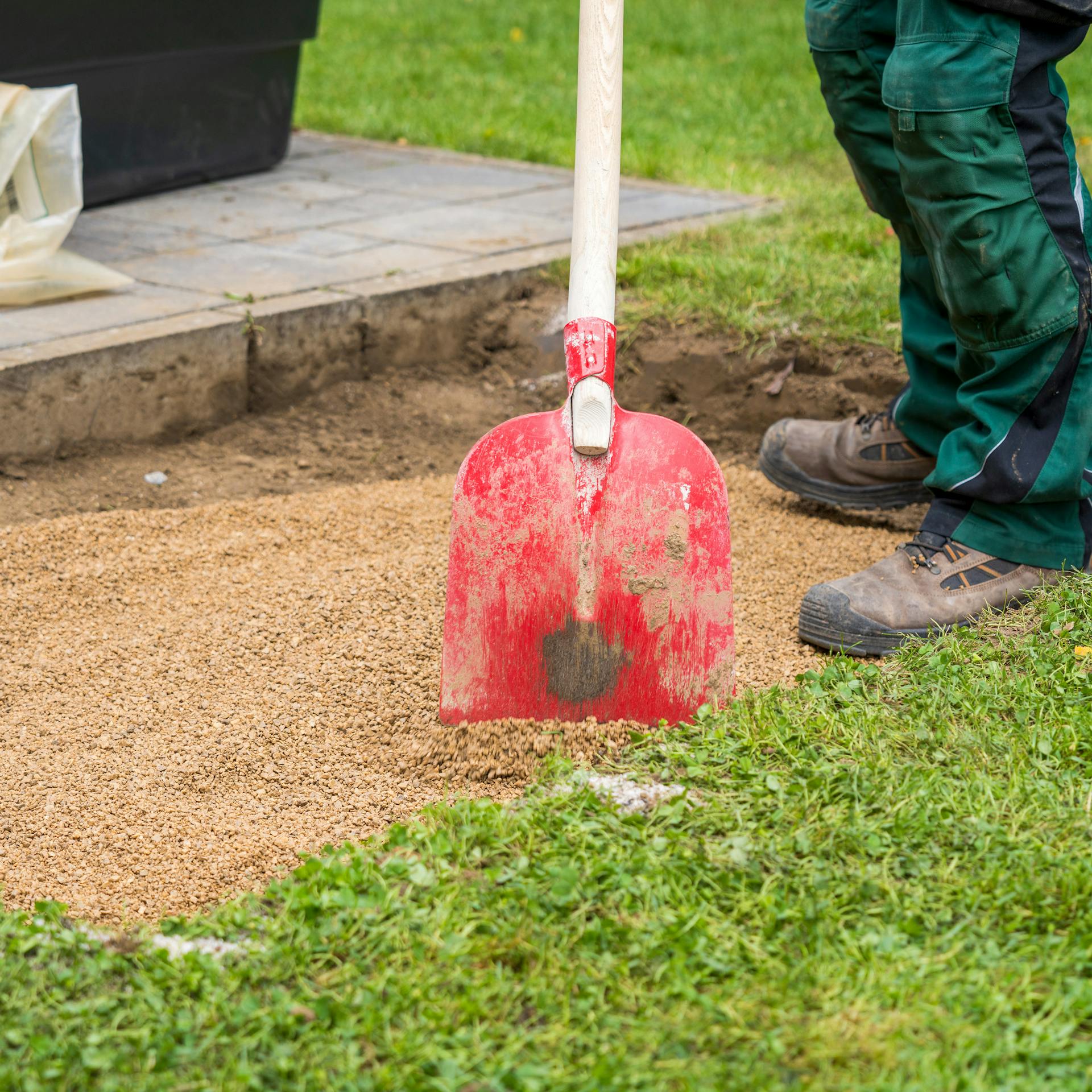 Heimwerker verteilt Splitt mit Schaufel in ausgehobener Fläche