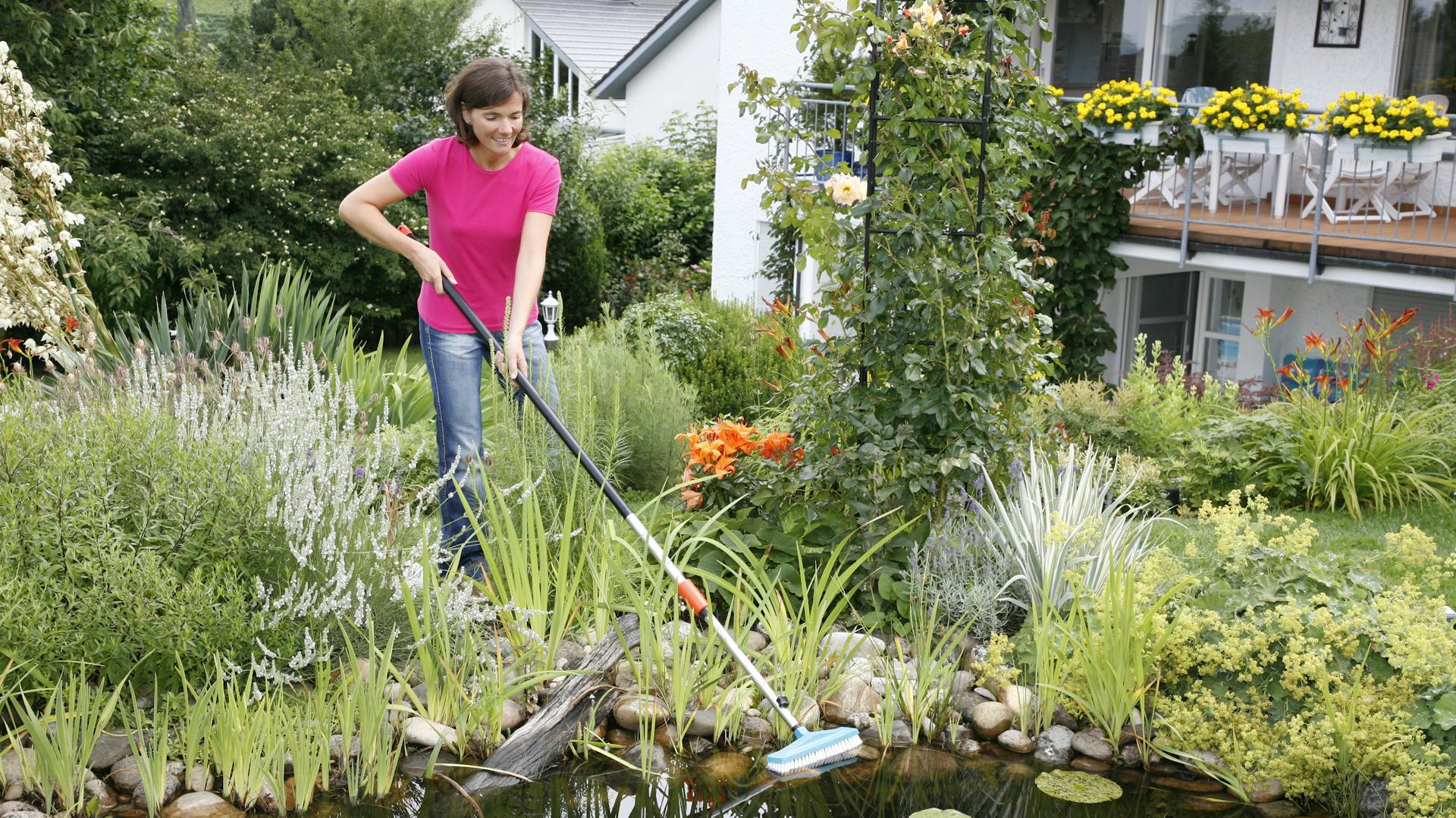 Eine Frau reinigt Gartenteich mit Teleskopreiniger