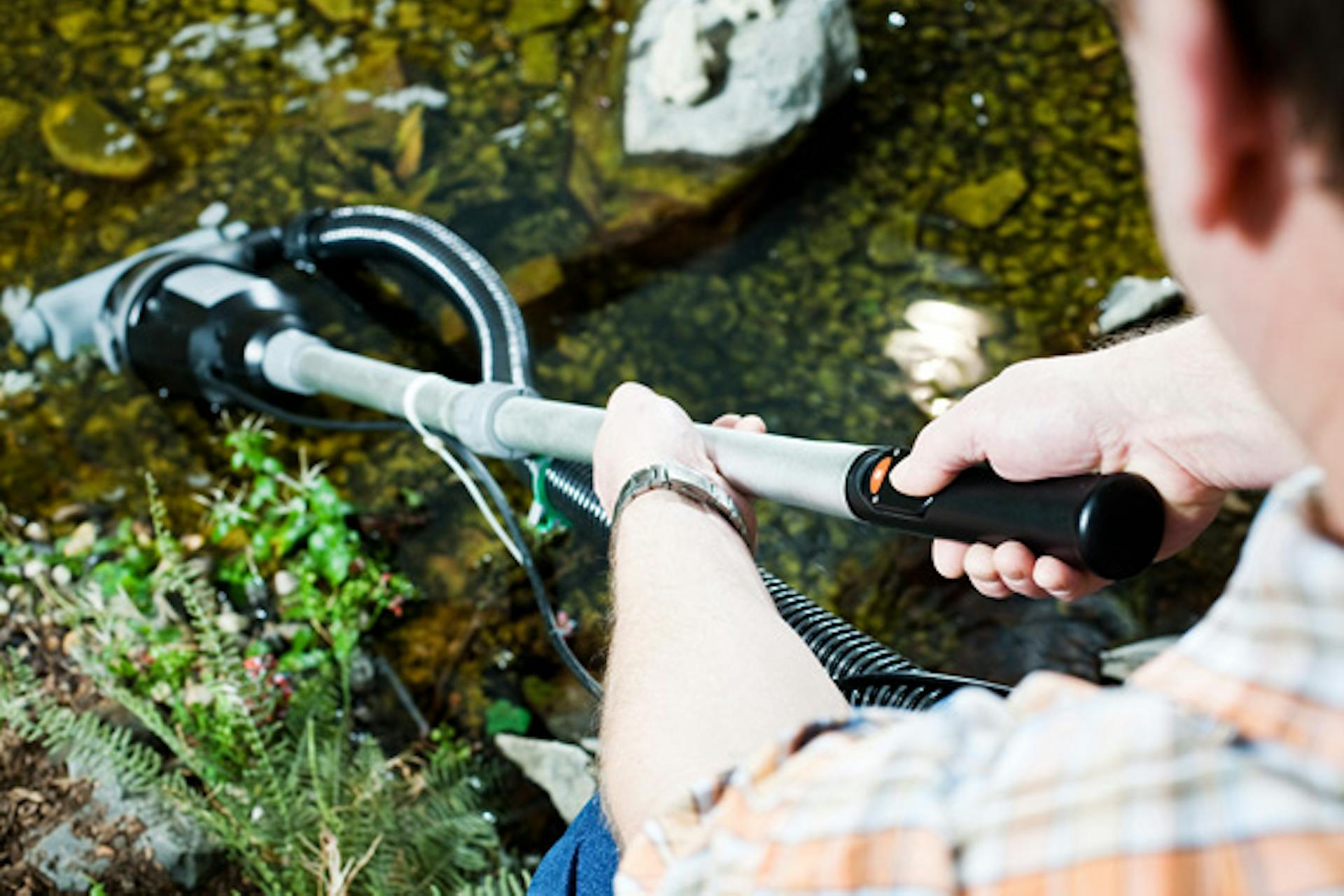 Gärtner reinigt Gartenteich mit Teichsauger.