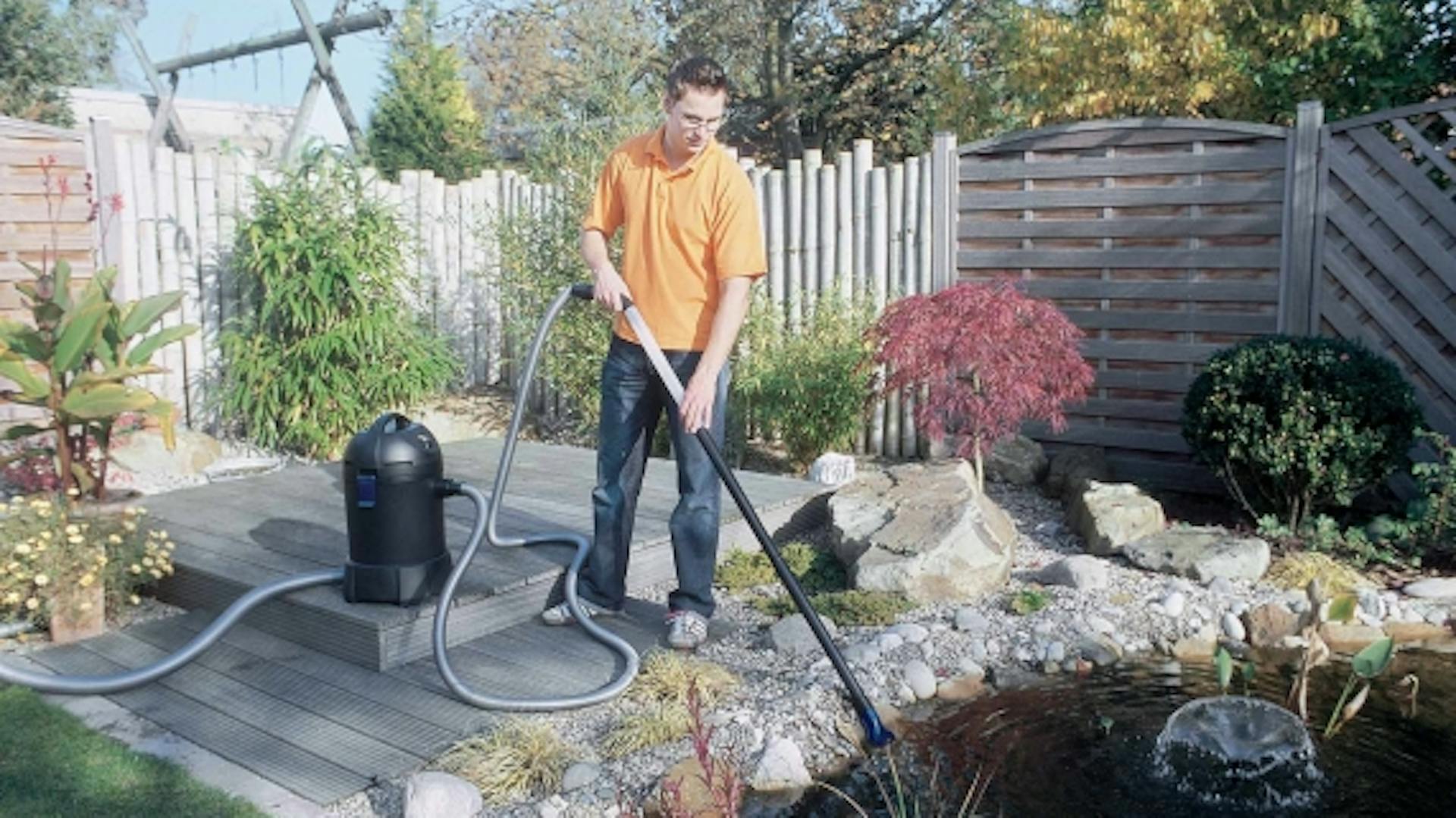 Mann mit Schlammsauger reinigt Teich