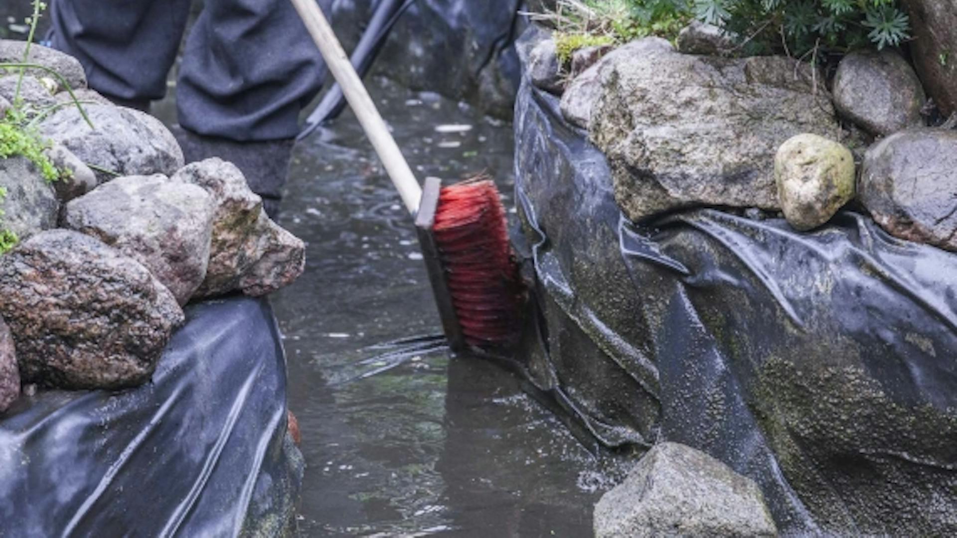 Mann reinigt Teichfolie mit Besen