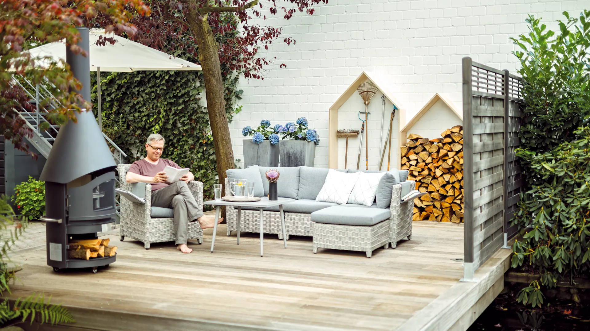 Foto di una terrazza in legno con mobili da giardino e forno di fronte a un fendivista e ombrellone