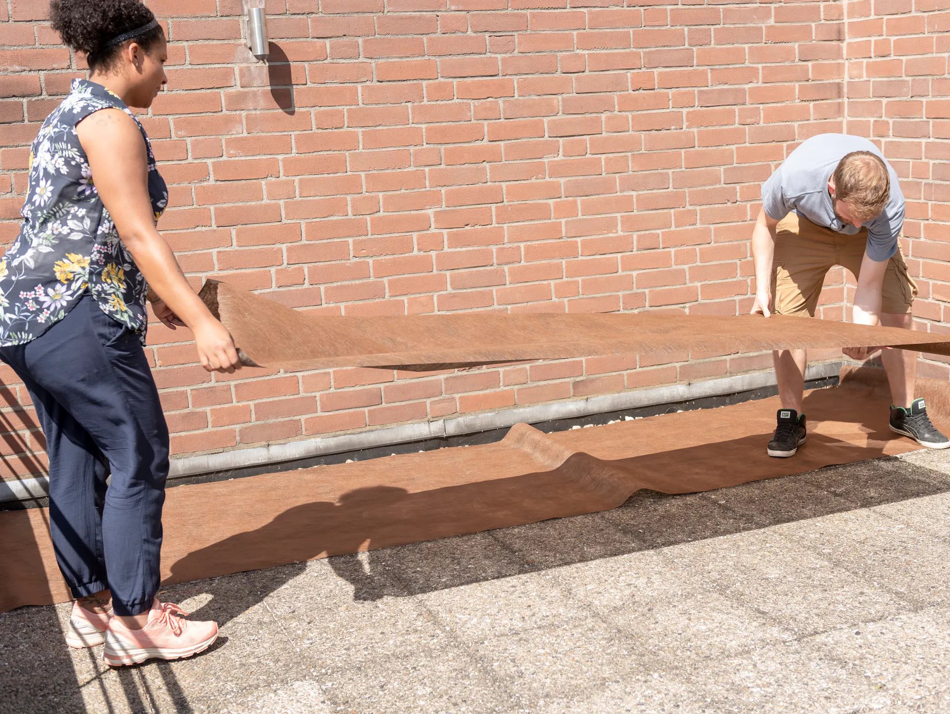 Zwei Menschen verlegen eine Plane auf bestehenden Steinplatten