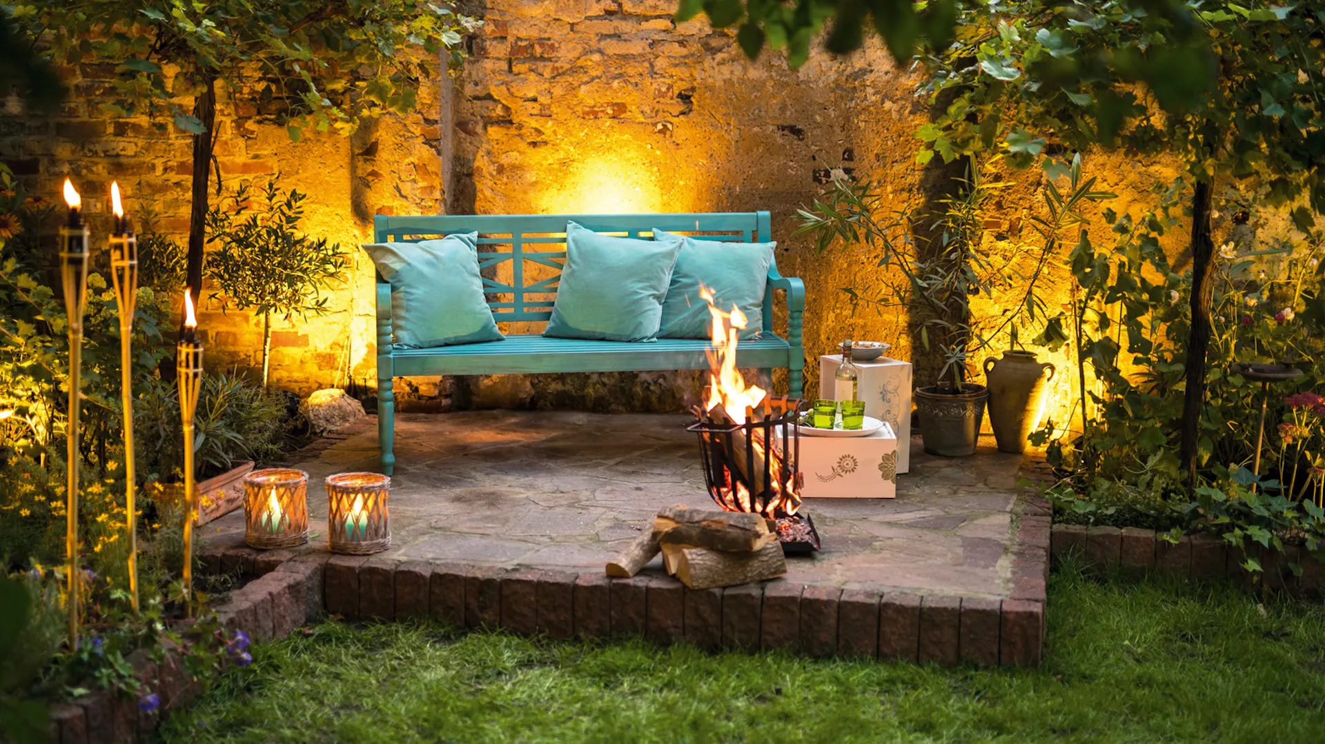 Eine Terrasse mit Hintergrundbeleuchtung, Fackeln und Sitzmöglichkeit.