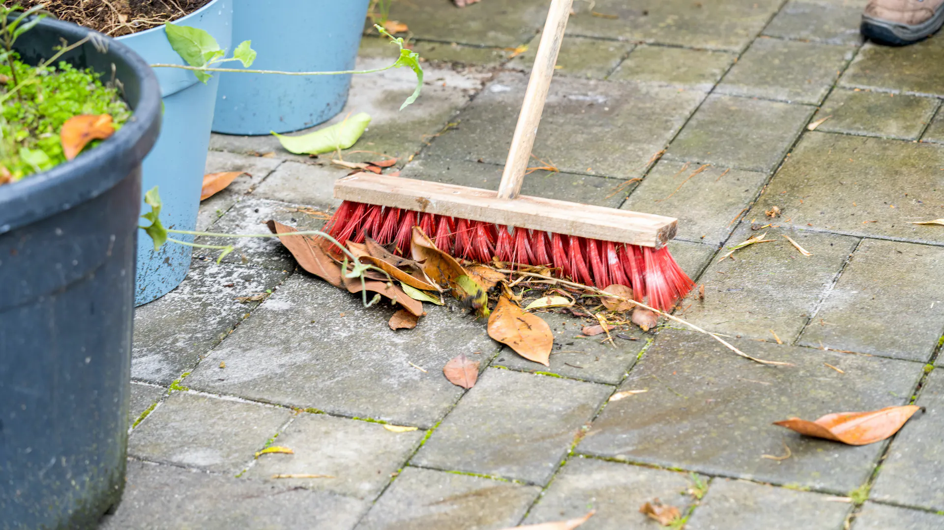 Terrassenplatten werden mit einem Besen gereinigt.