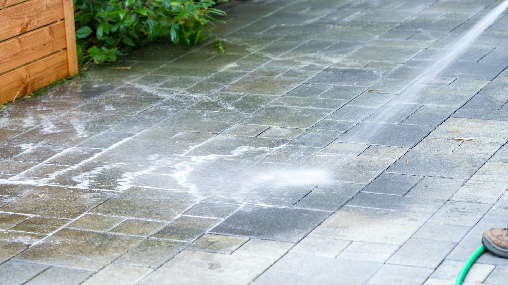 Jemand reinigt die Terrasse mit einem Hochdruckreiniger.