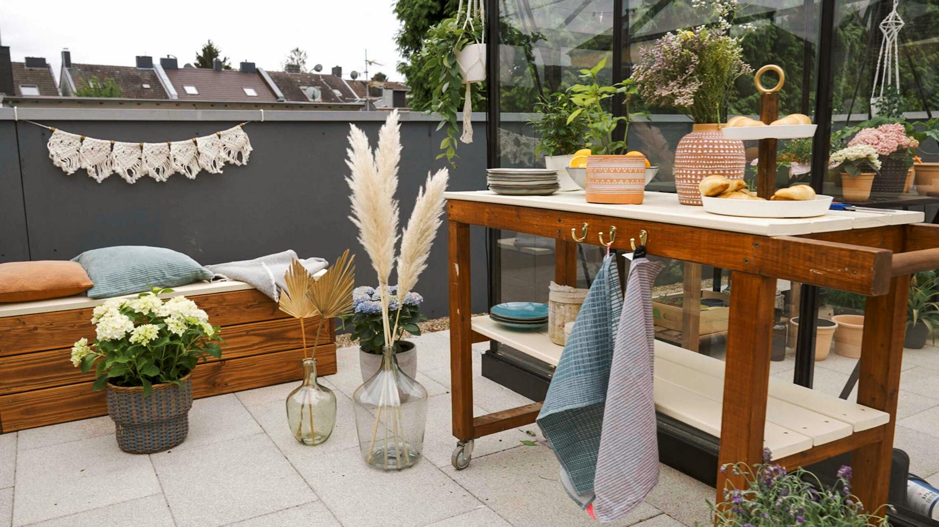 Bank Alfred und Servierwagen Sophie stehen auf einer mit Vasen und Trockenblumen geschmückten Dachterrasse.