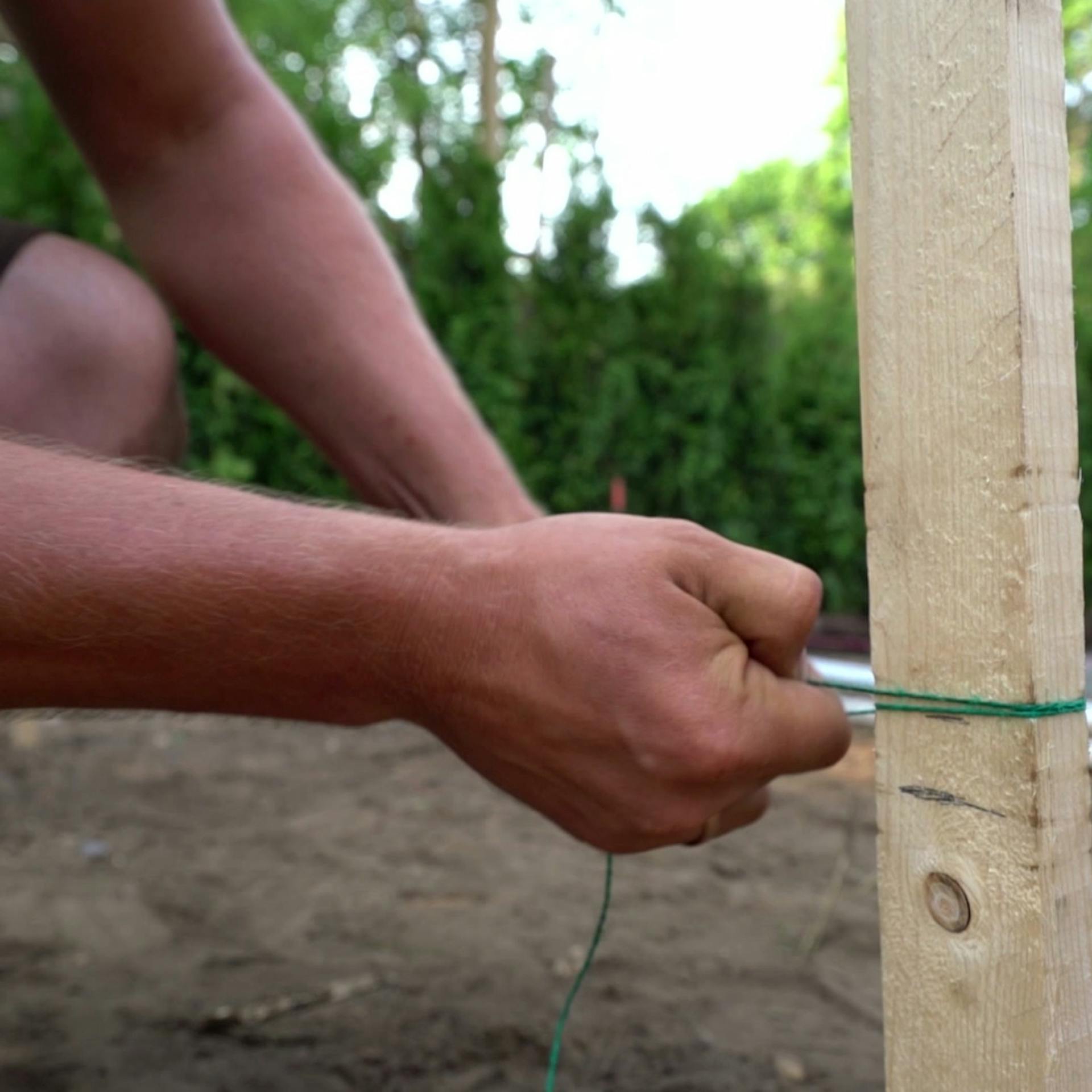 Osoba viaže špagát k drevenému kolíku zapichnutému do zeme, aby vyznačila priebeh terasy.