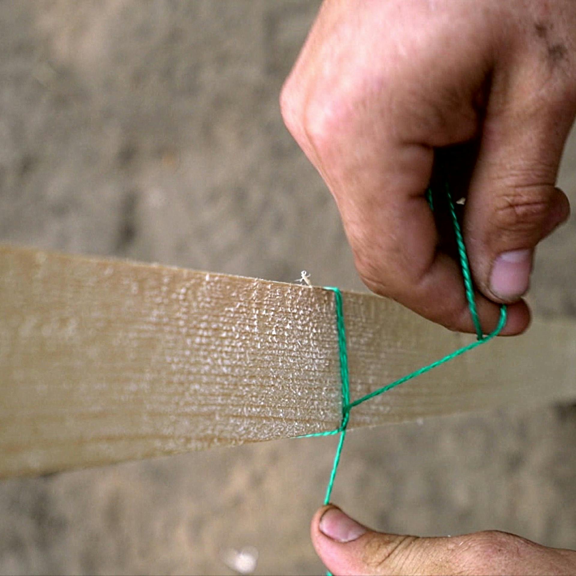 Foto zweier Hände, die eine Schnur um einen Holzpflock ziehen und so einen gestochenen Mastwurfknoten umsetzen
