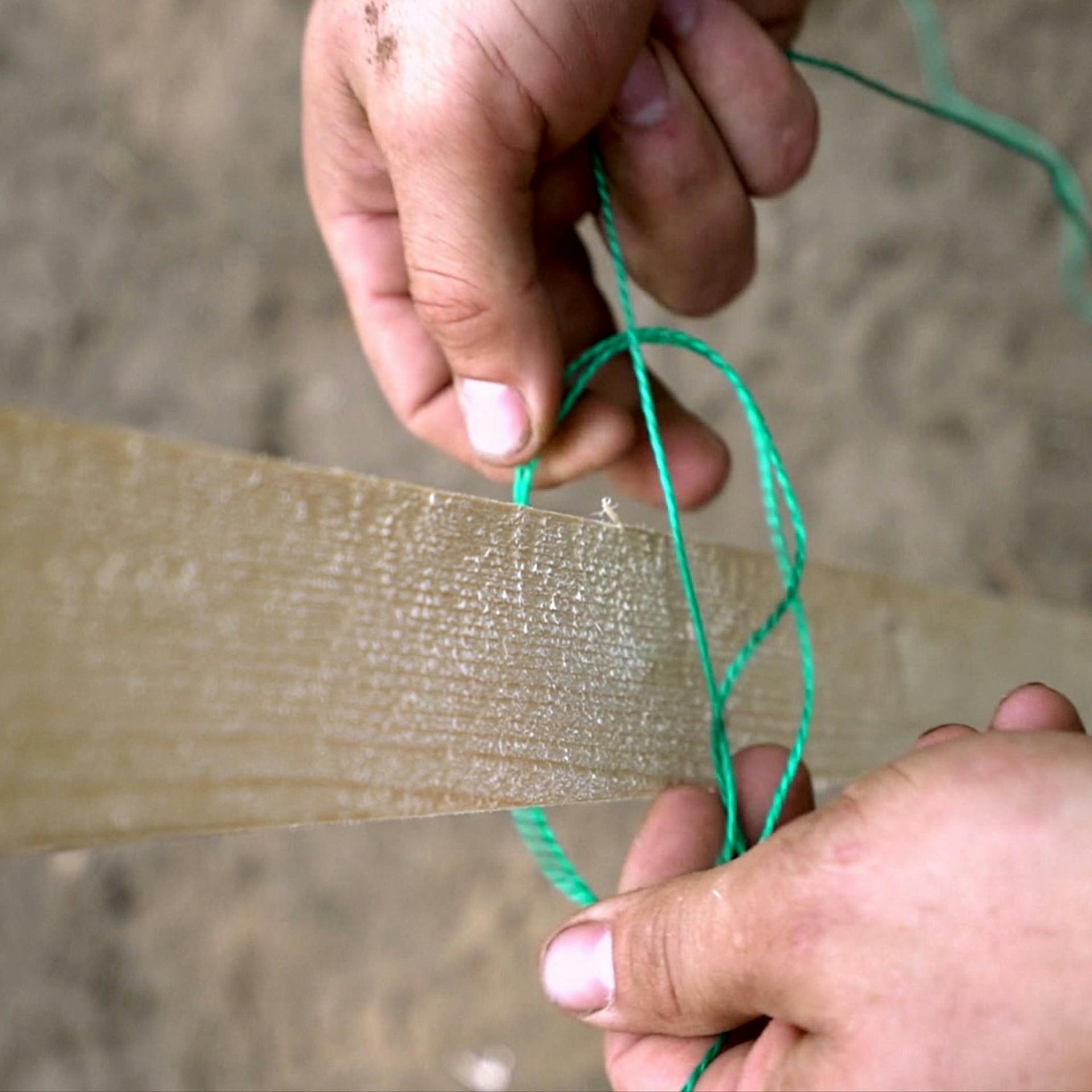Foto zeigt Hände, die eine Schnur an einem Holzpfosten für einen gestochenen Mastwurf befestigen