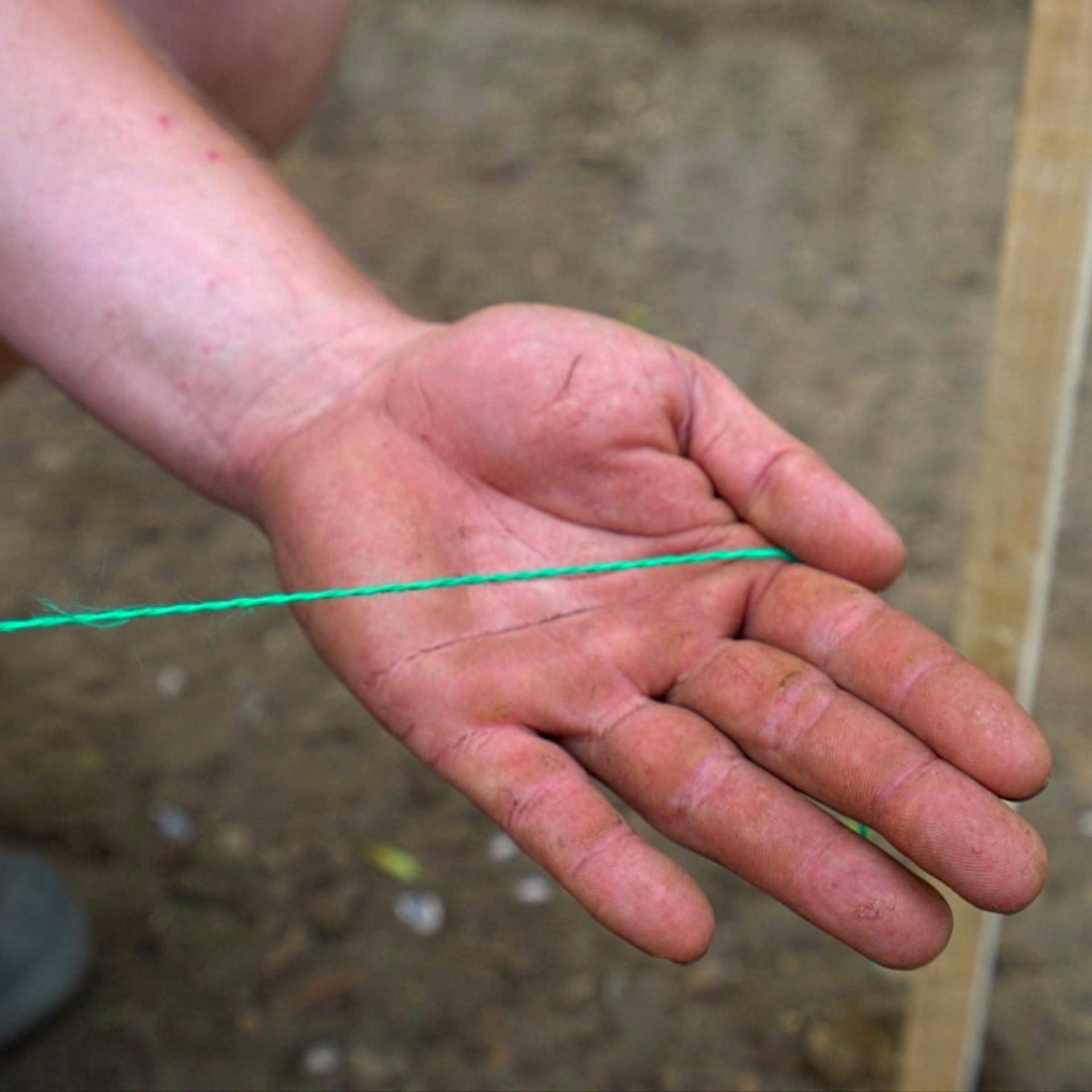 Foto einer Hand mit grüner Schnur für den gestochenen Mastwurf