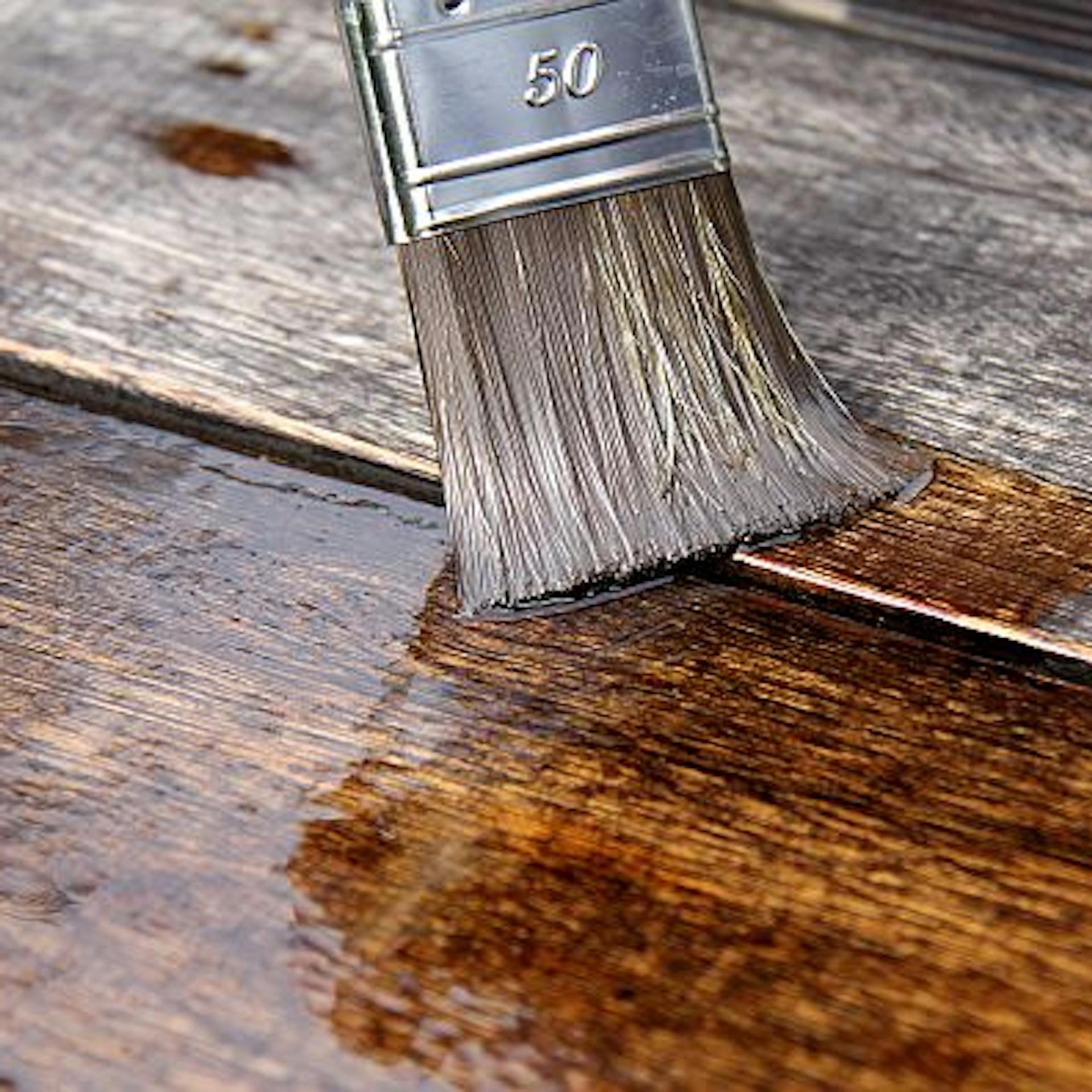 Jemand streicht Holzbretter mit einem Pinsel und einer Holzlasur.