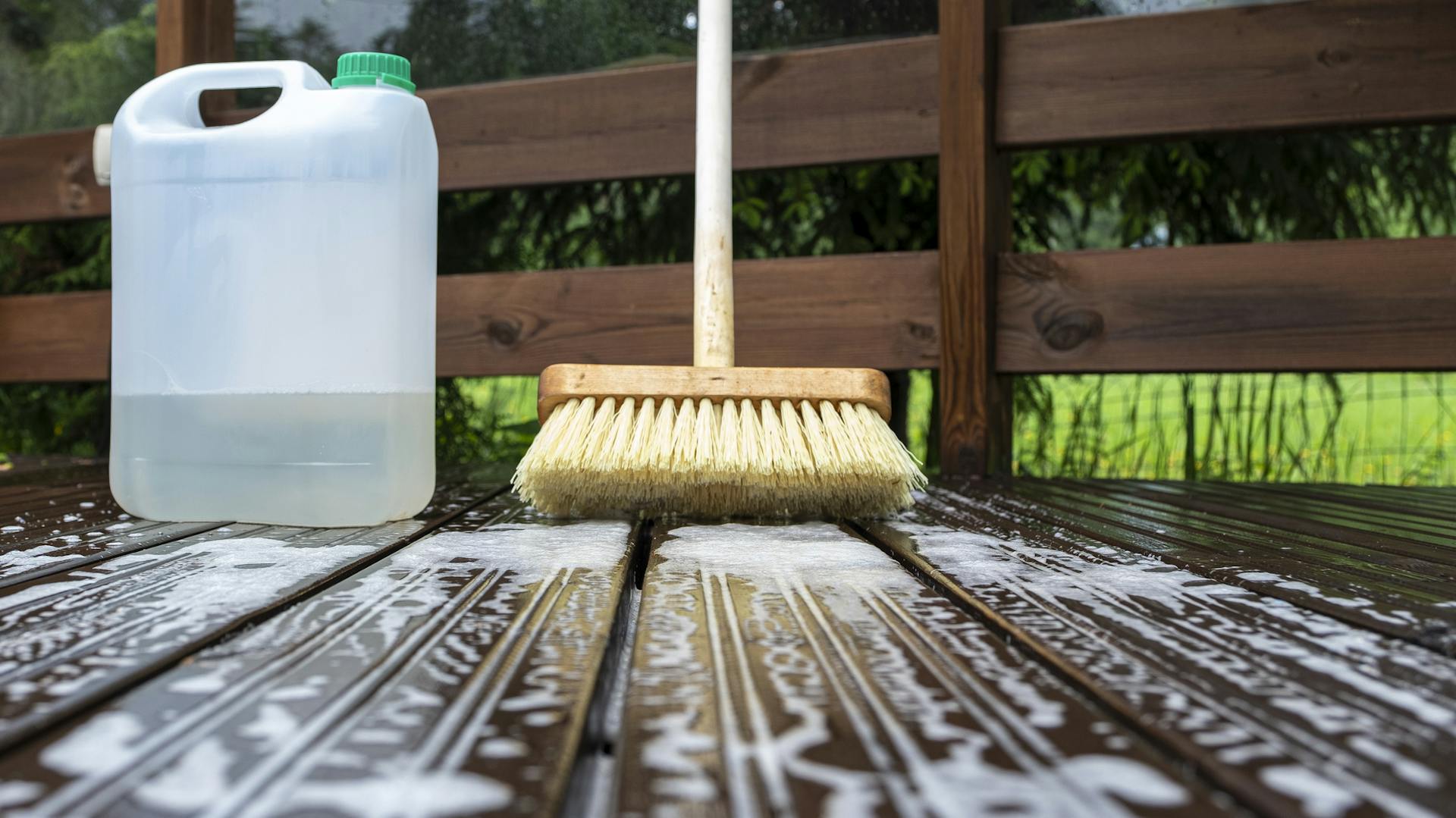 Besen mit Reinigungsmittel auf einer Holzterrasse