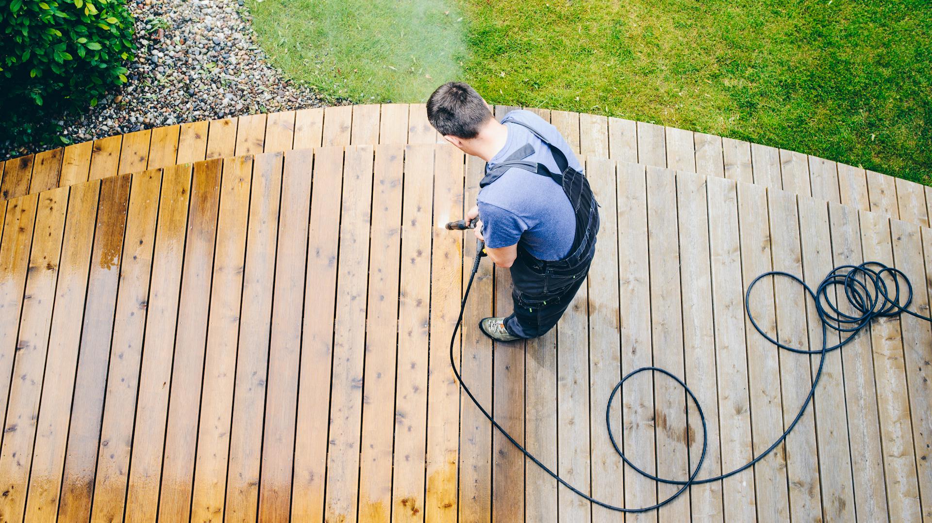 Il terrazzo in legno viene pulito da una persona con stivali di gomma con un’idropulitrice ad alta pressione.