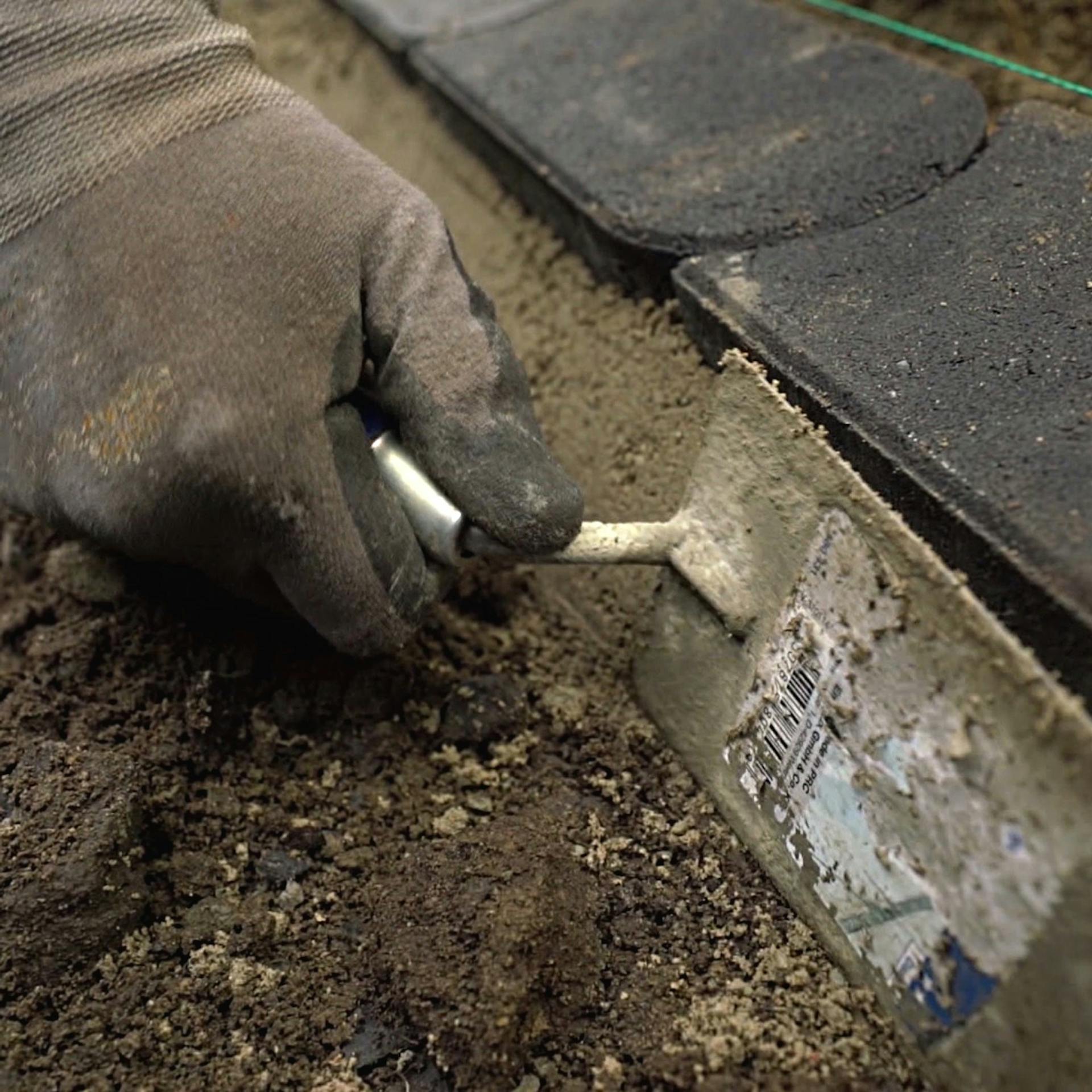 Foto vom Anlegen einer Mähkante mit einer Rückenstütze aus Beton, die von einem Heimwerker mit einer Maurerkelle bearbeitet wird