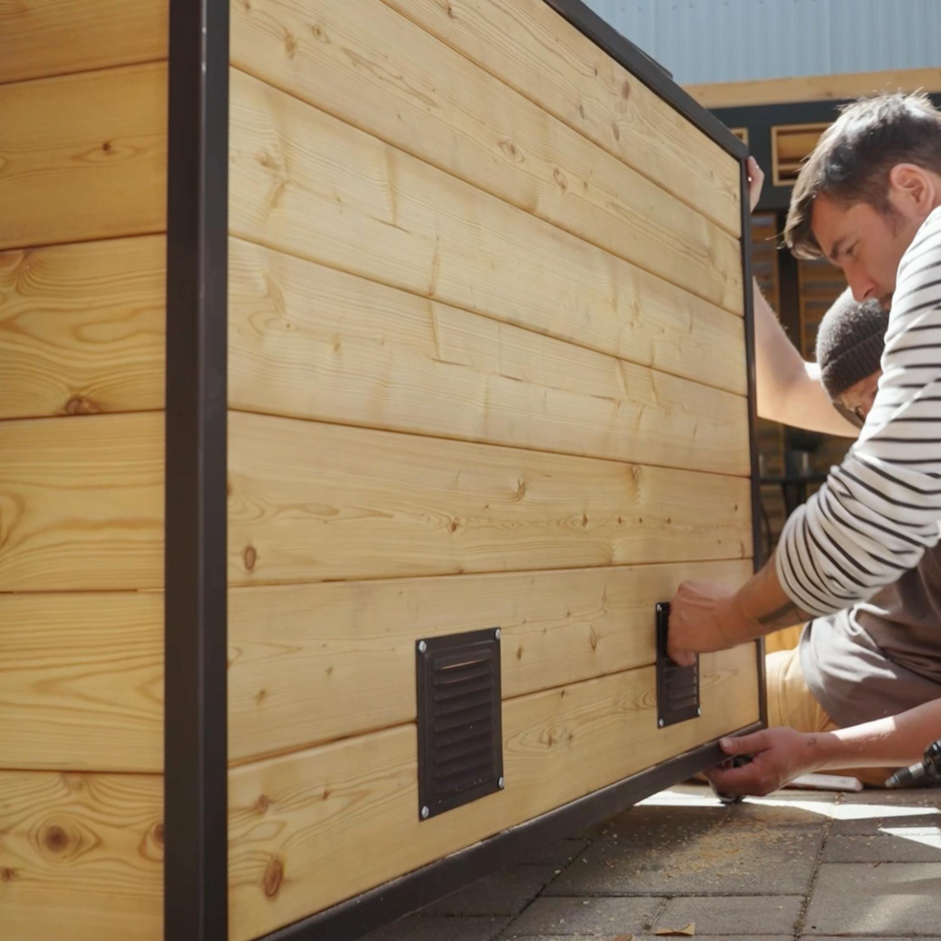 Un uomo installa una griglia di aerazione sul retro della cucina esterna.
