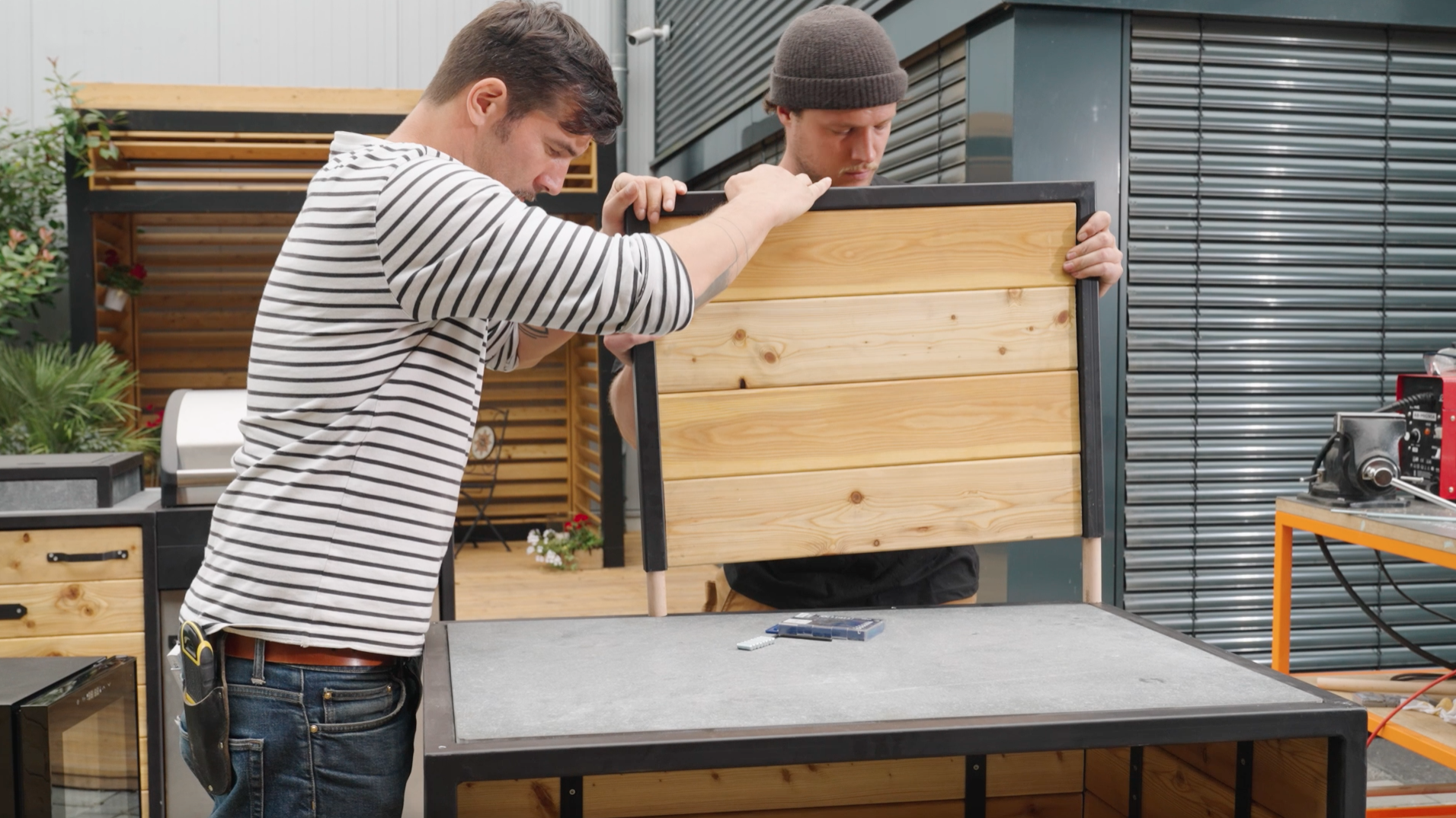 Due uomini fissano le pareti posteriori finite sui perni di legno rotondo che collegano le pareti posteriori al corpo della cucina esterna.