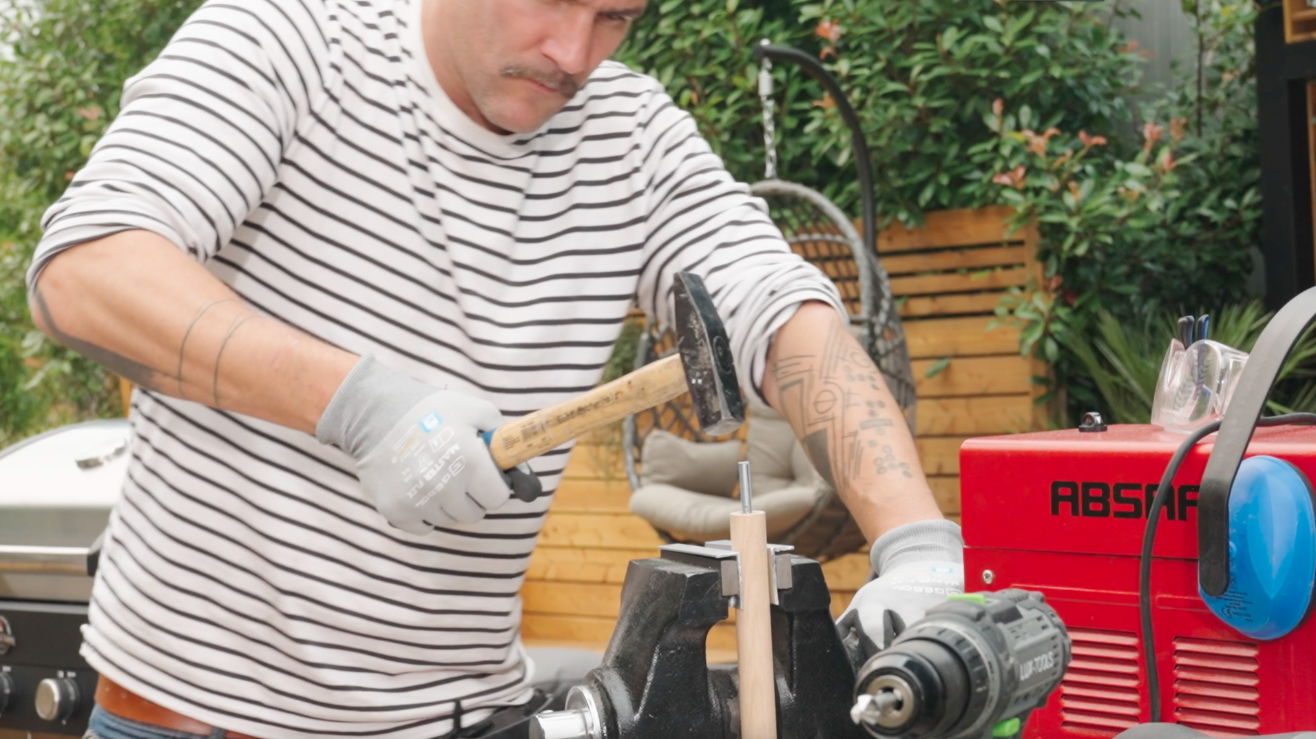 Un uomo usa un martello per spingere una barra filettata in un tronco tondo bloccato in una morsa.