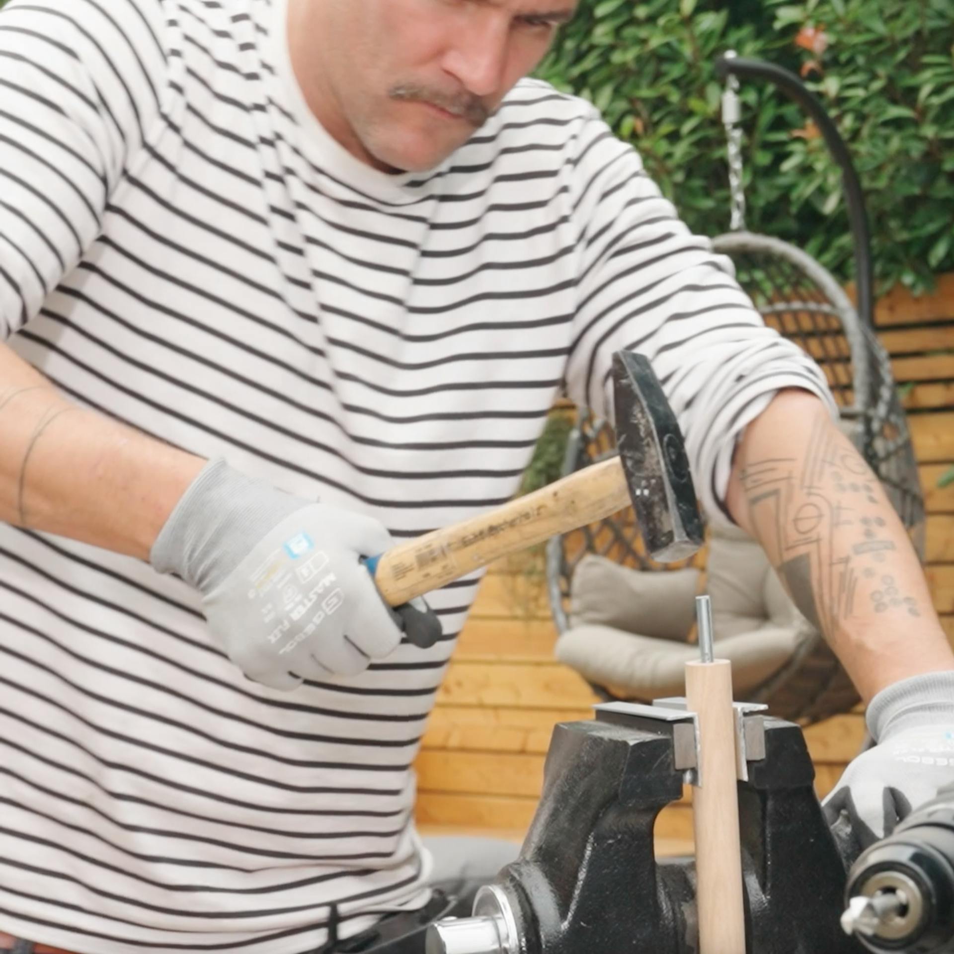 Un uomo usa un martello per spingere una barra filettata in un tronco tondo bloccato in una morsa.